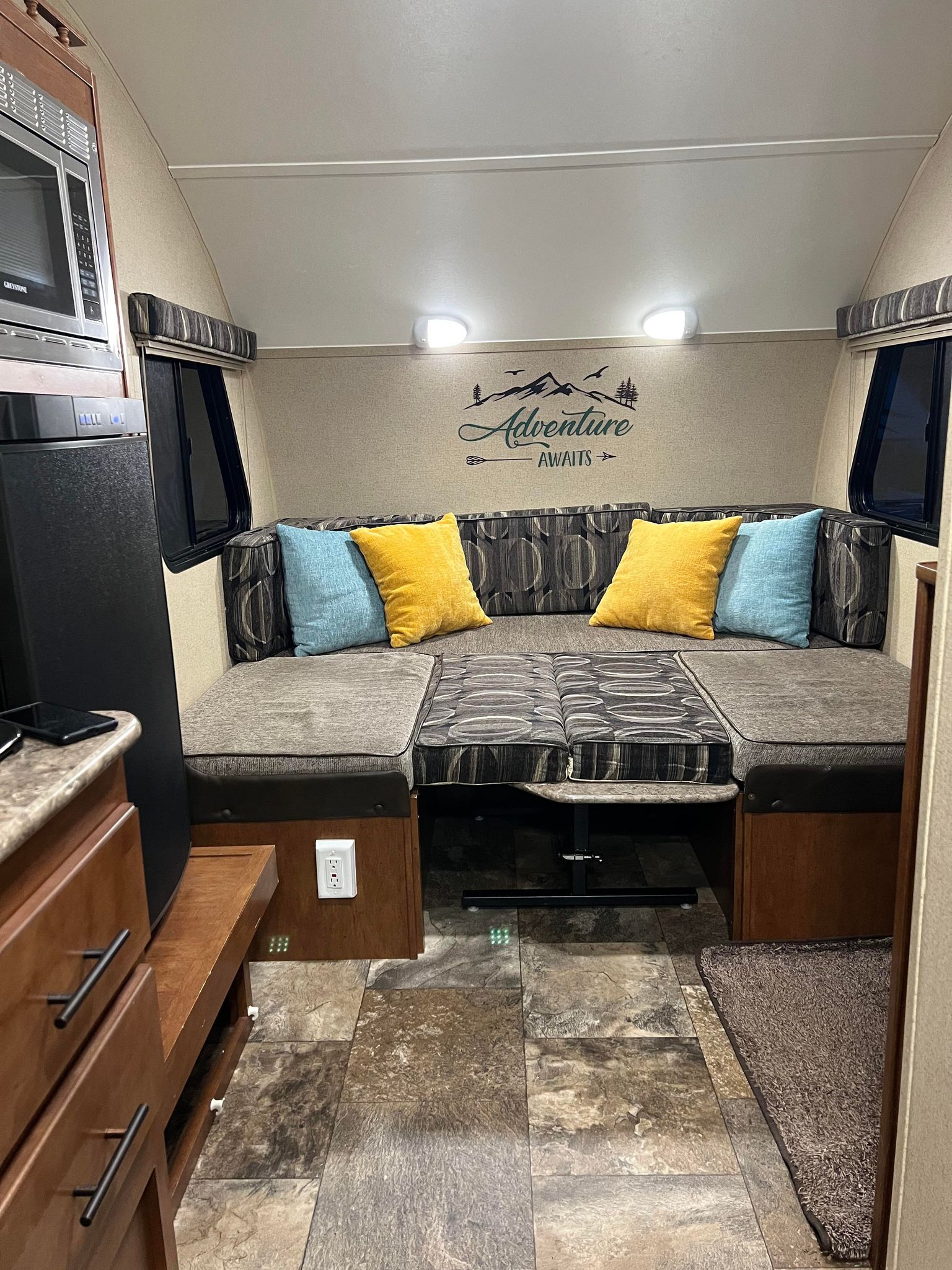 RV rental interior featuring a cozy dinette with U-shaped seating, "Adventure Awaits" decor, microwave, and fridge.. Forest River R-Pod 2015