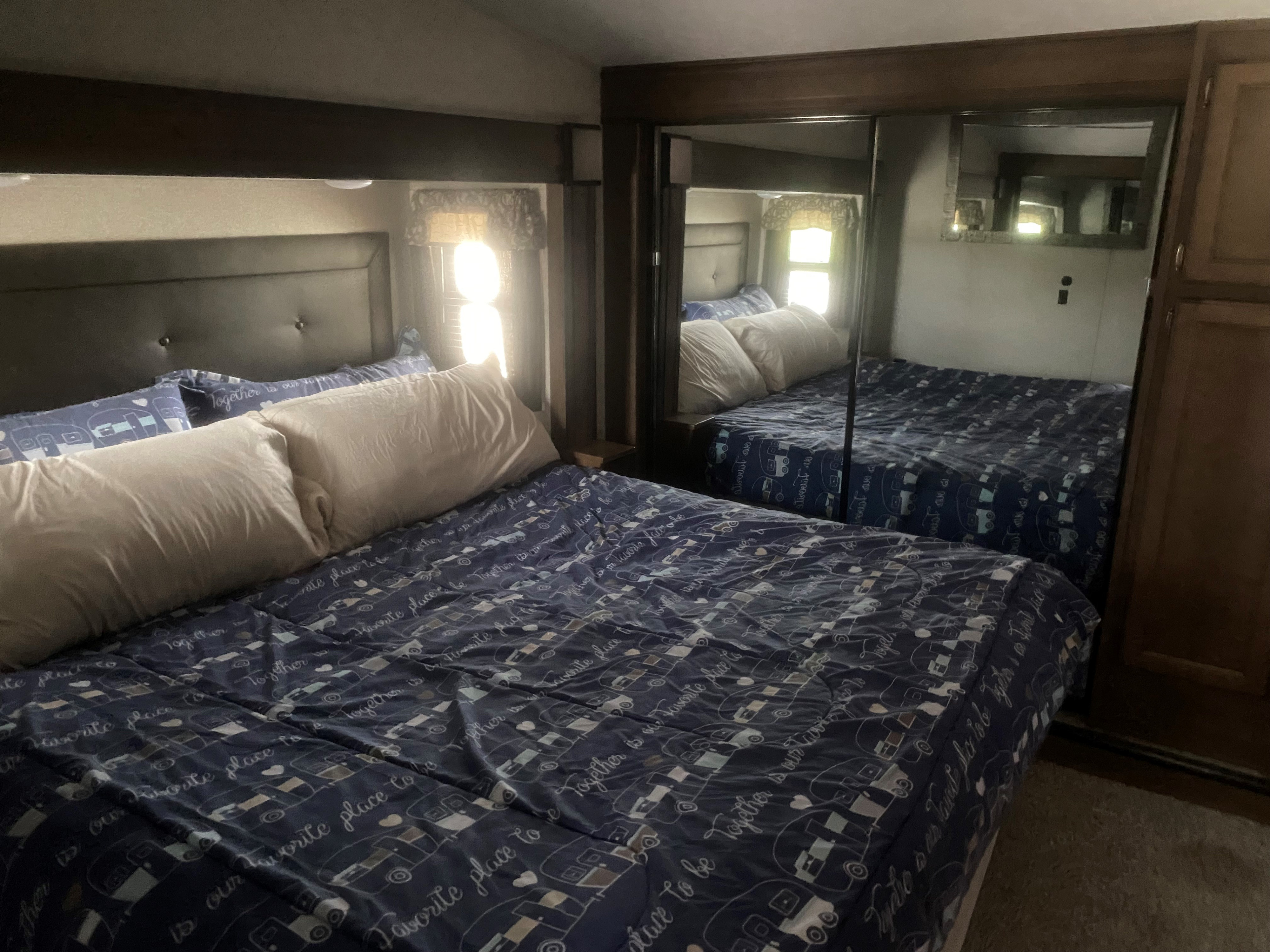 Step into comfort! This RV bedroom, ideal for an RV rental, features a cozy bed with camper-themed linens & mirrored closet.. Keystone RV Cougar 2019