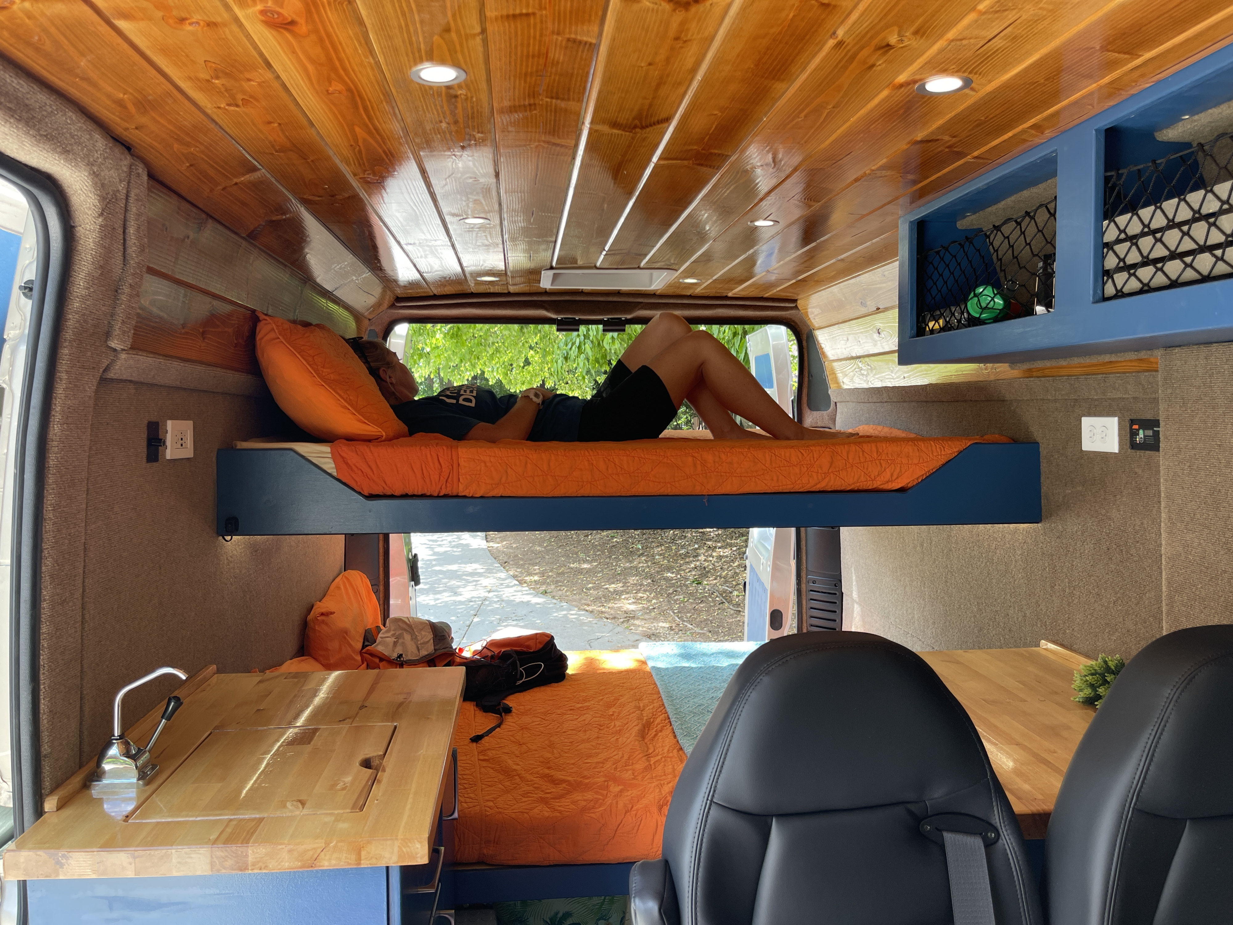 RV rental interior with a person on the top bunk, a lower bed, a kitchen counter, and a beautiful wood ceiling.. Ram Promaster 2021