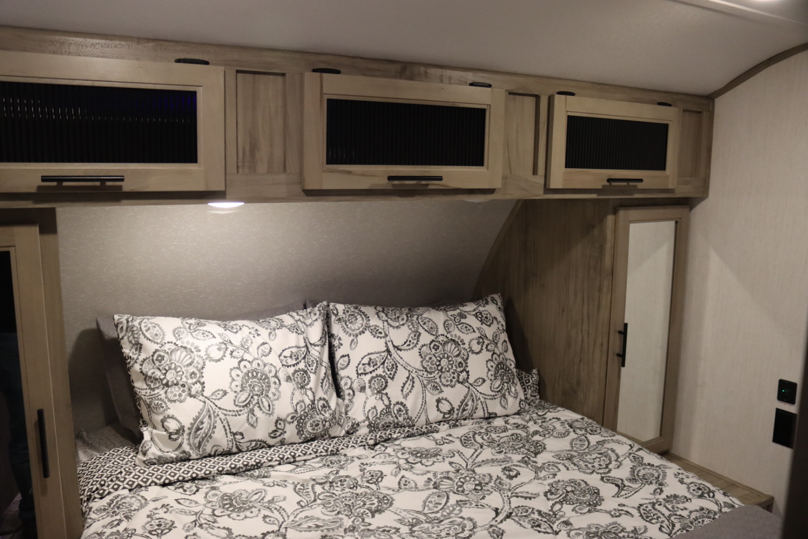 Cozy RV rental bedroom with patterned bedding, overhead cabinets, and built-in storage, ideal for compact travel.. Forest River Cherokee Alpha Wolf 2022