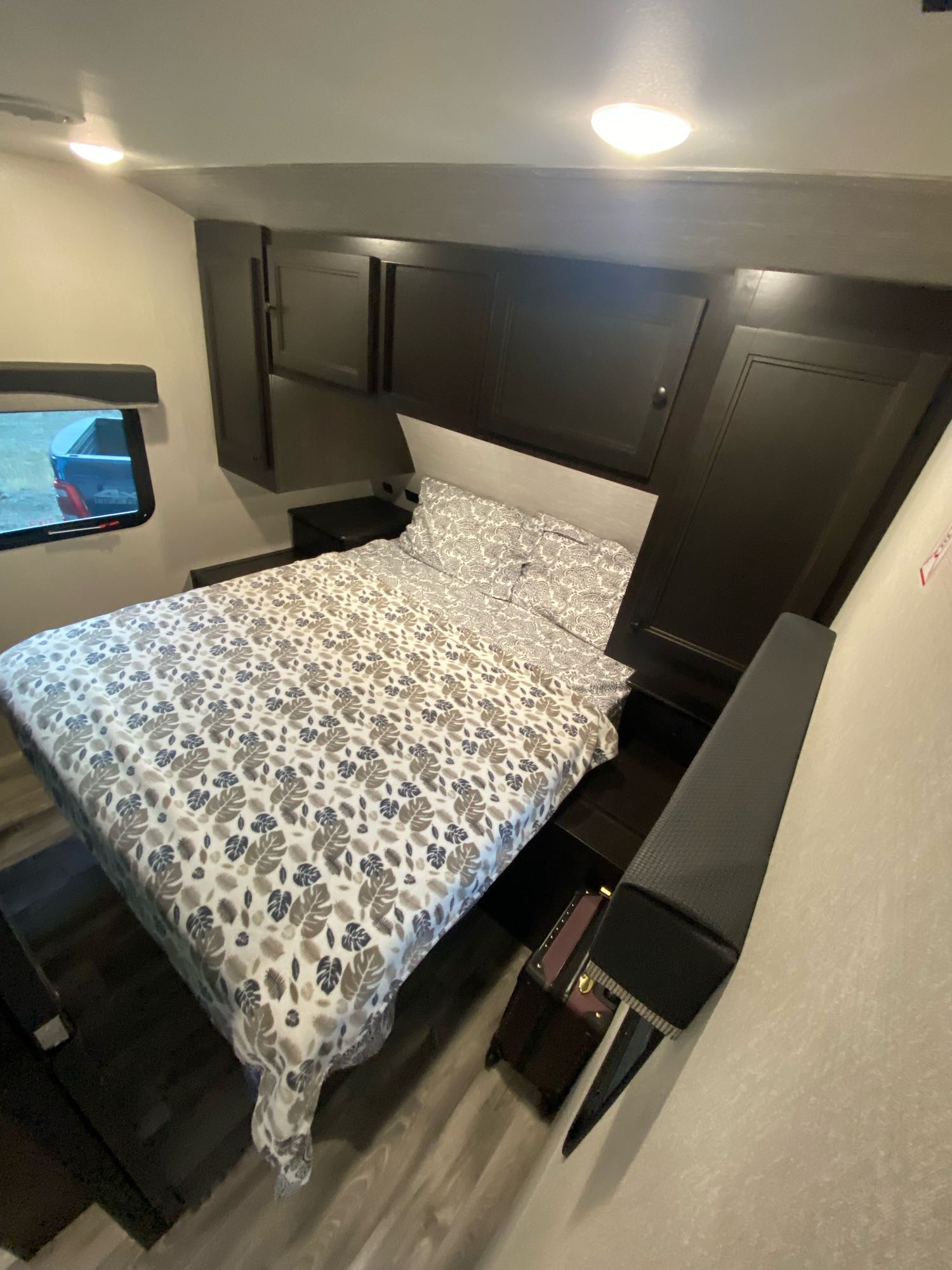 Cozy RV rental bedroom with leaf-patterned bedding, dark cabinets, and a window viewing a truck. Brightly lit interior.. Starcraft Super Lite 2022