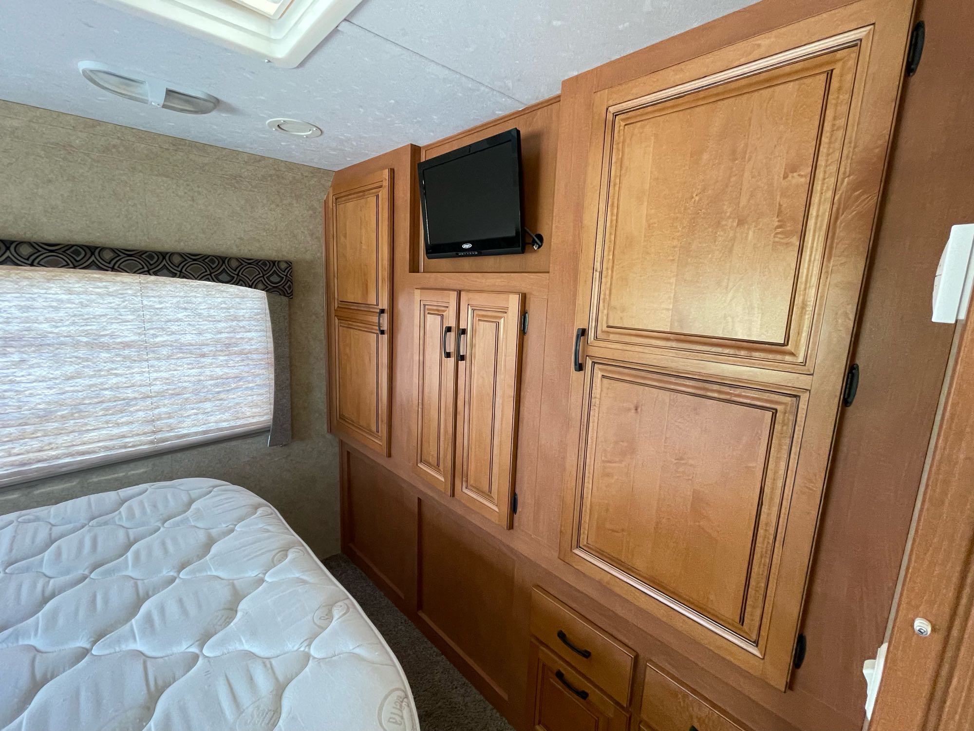 Inside an RV rental: a compact bedroom featuring a comfortable mattress, window with blinds, and built-in wood cabinets with a TV.. Forest River Sunseeker 2013