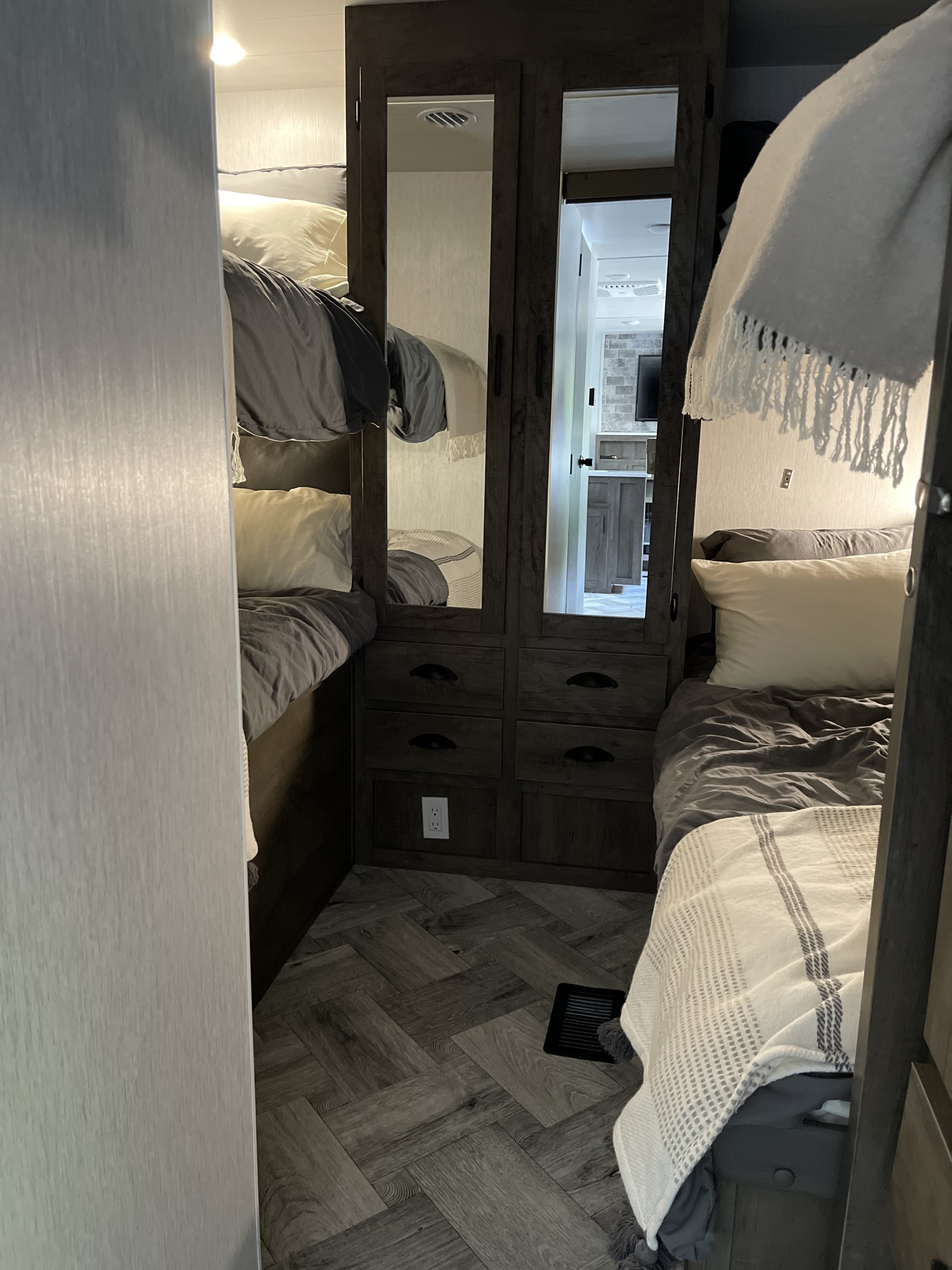 Cozy RV rental interior with bunk beds, a central mirrored storage unit, and herringbone flooring.. Forest River Evo T2990 2022