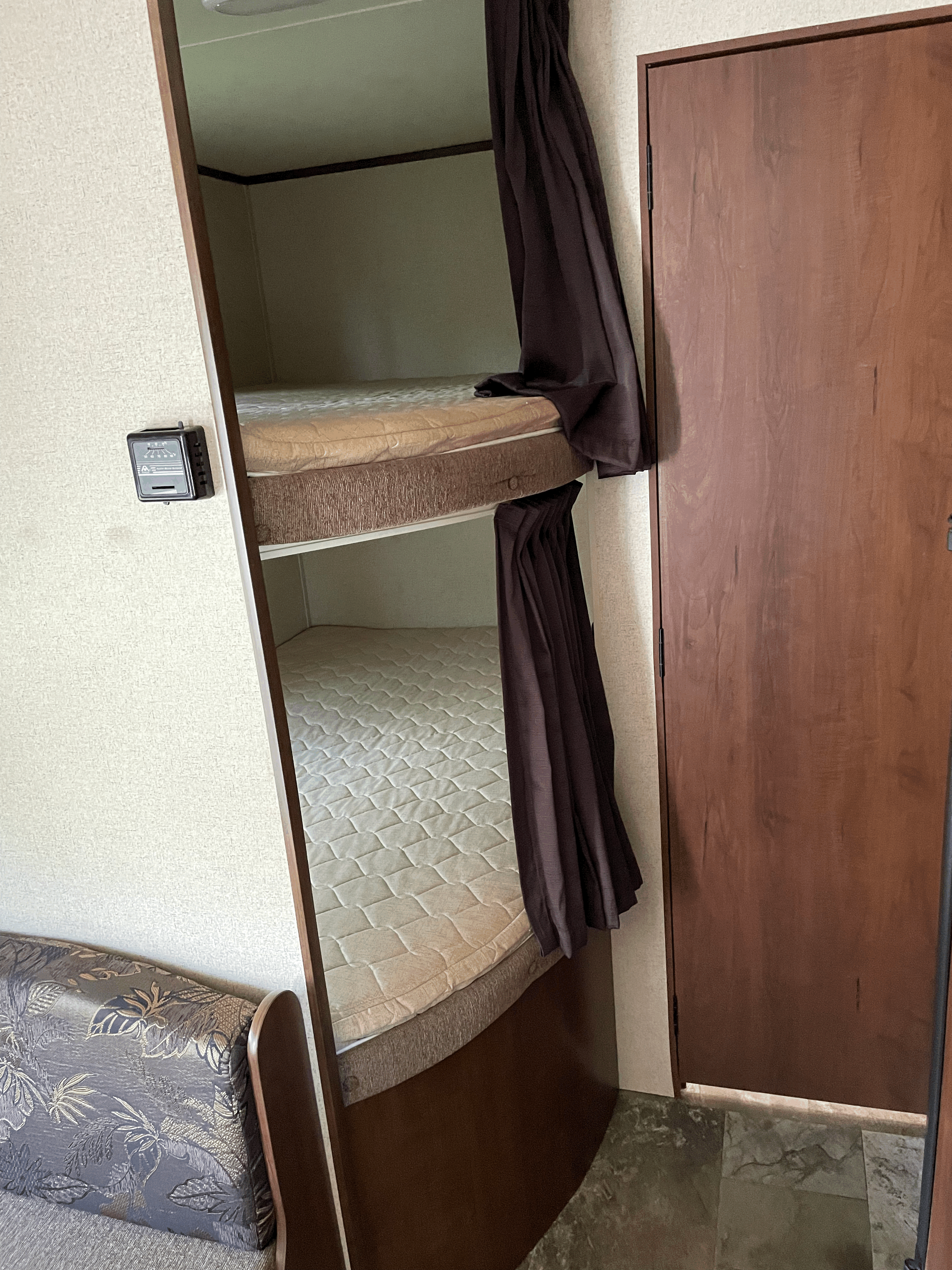 RV rental interior with cozy bunk beds and curtains, a thermostat on the wall, and a patterned couch, ideal for families.. Jayco Jay Feather Ultra Lite SLX 2015