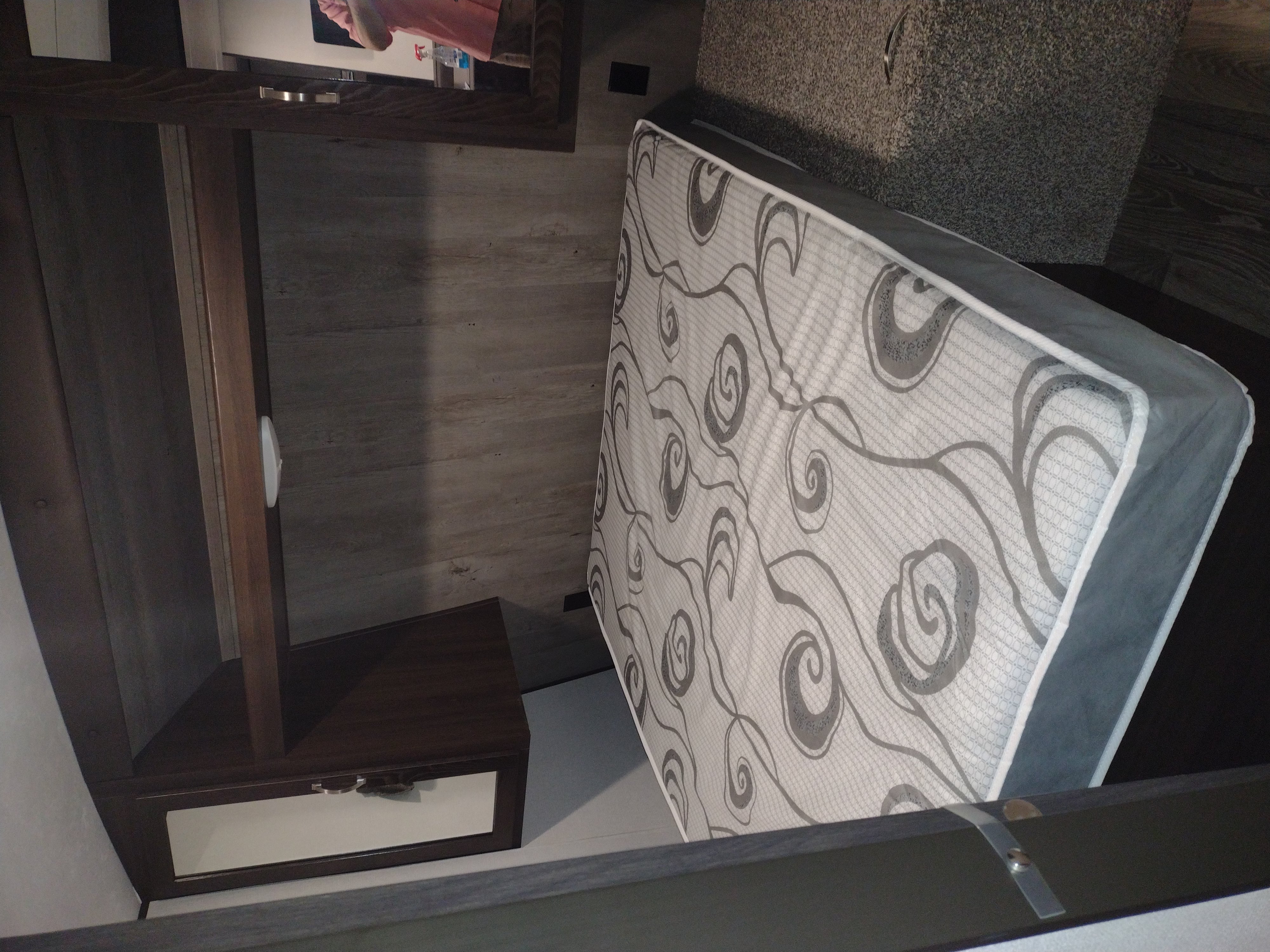 RV rental bedroom showcasing a patterned mattress, dark wood-grain walls, and a built-in nightstand.. Keystone Springdale 2020