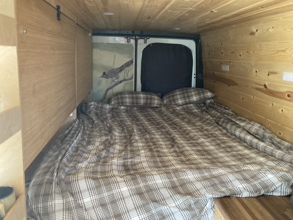 This **RV rental** features a cozy sleeping area with plaid bedding, wood-paneled walls, and roadrunner artwork.. Dodge Sprinter 2003