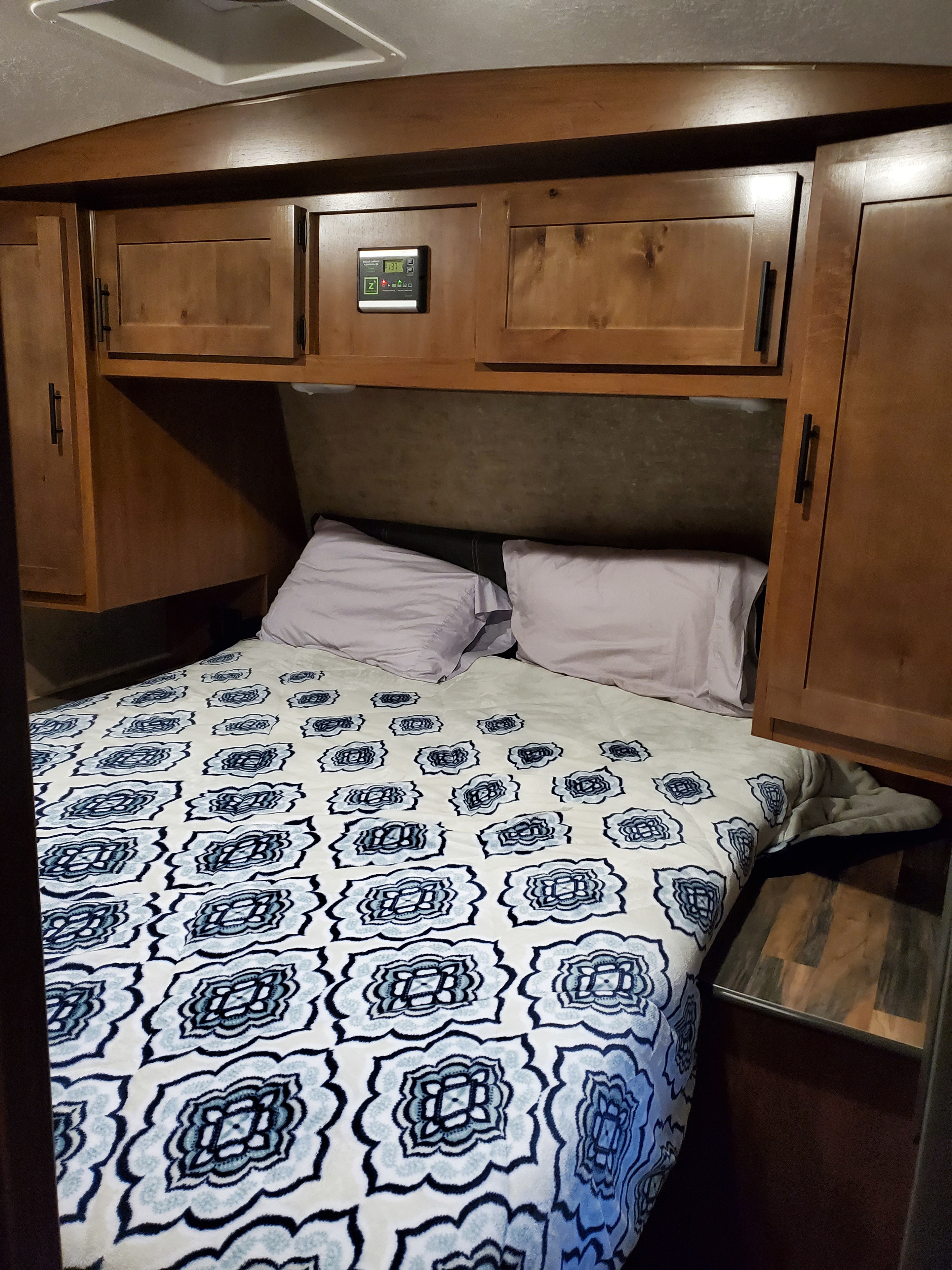 RV rental interior: A neatly made bed with a blue pattern, wood cabinets, and power display.. Outdoors RV Timber Ridge 2022
