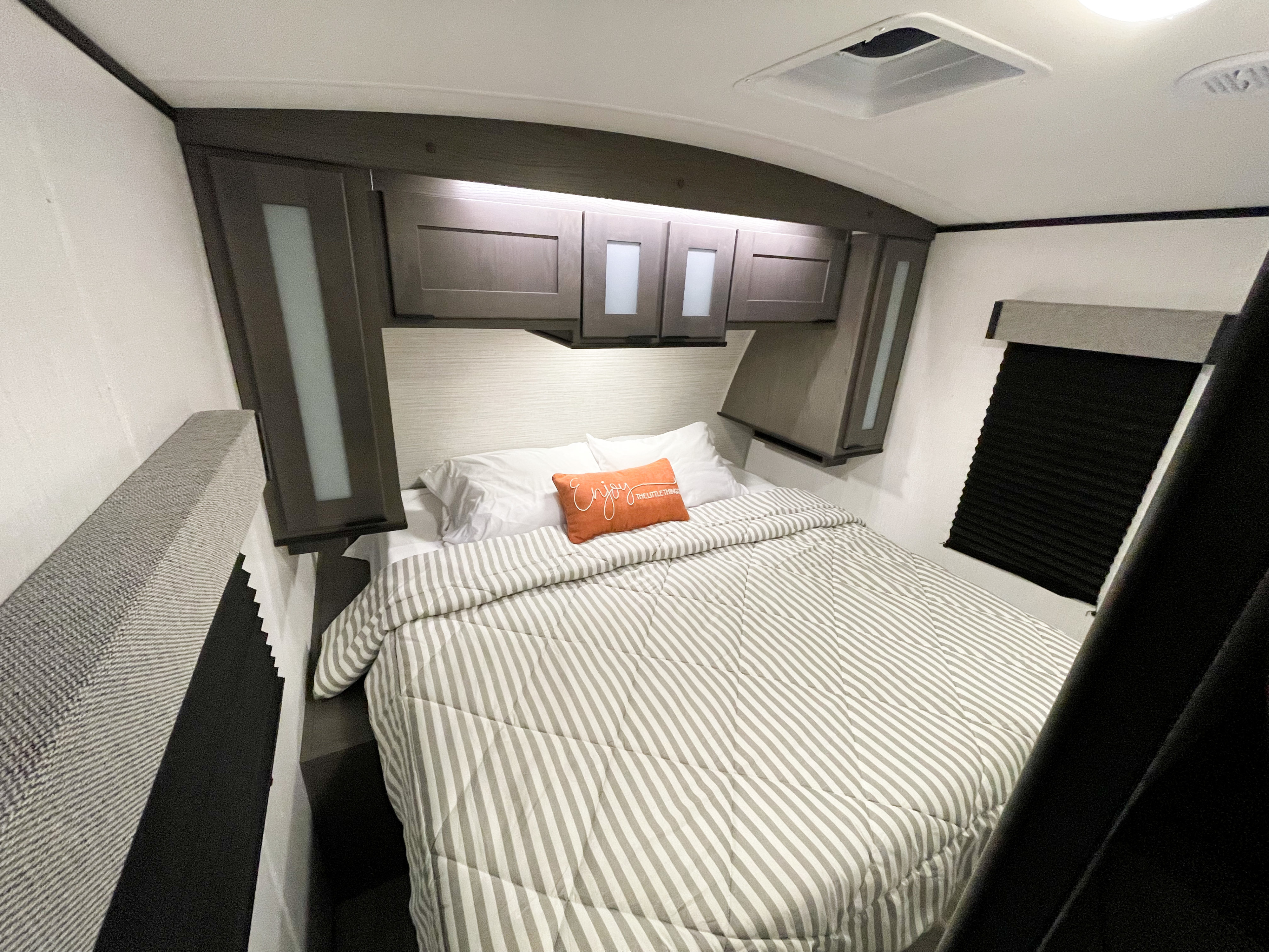 Cozy RV rental bedroom featuring a queen bed with striped comforter, overhead cabinets, and window blind for privacy.. Cruiser RV MGP 3100BH 2022