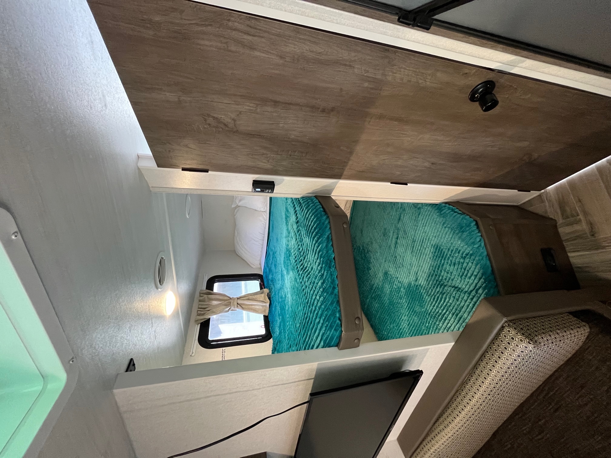 RV rental interior: two cozy bunk beds with teal blankets, a small window, and TV below, for compact living.. Forest River Salem Cruise Lite 2021