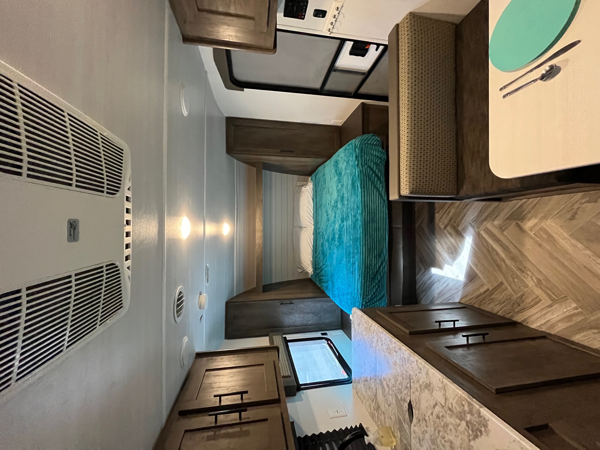 Inside this RV rental: bedroom with teal blanket, dining area, kitchen counter, and wood-patterned floor.. Forest River Salem Cruise Lite 2021