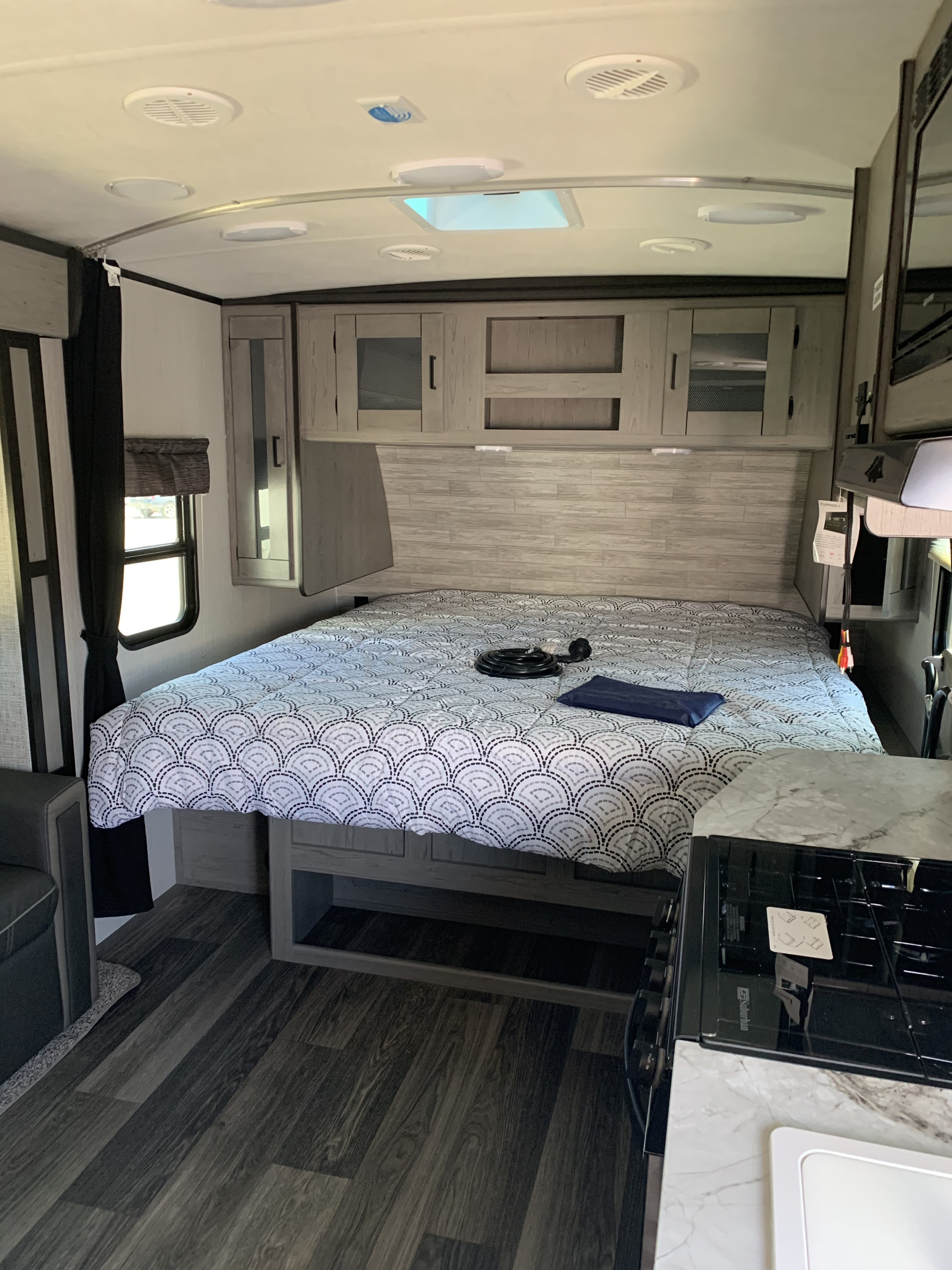 Cozy RV rental interior: Bedroom with bed, overhead cabinets, and compact kitchen corner.. Heartland RVs Mallard 2021