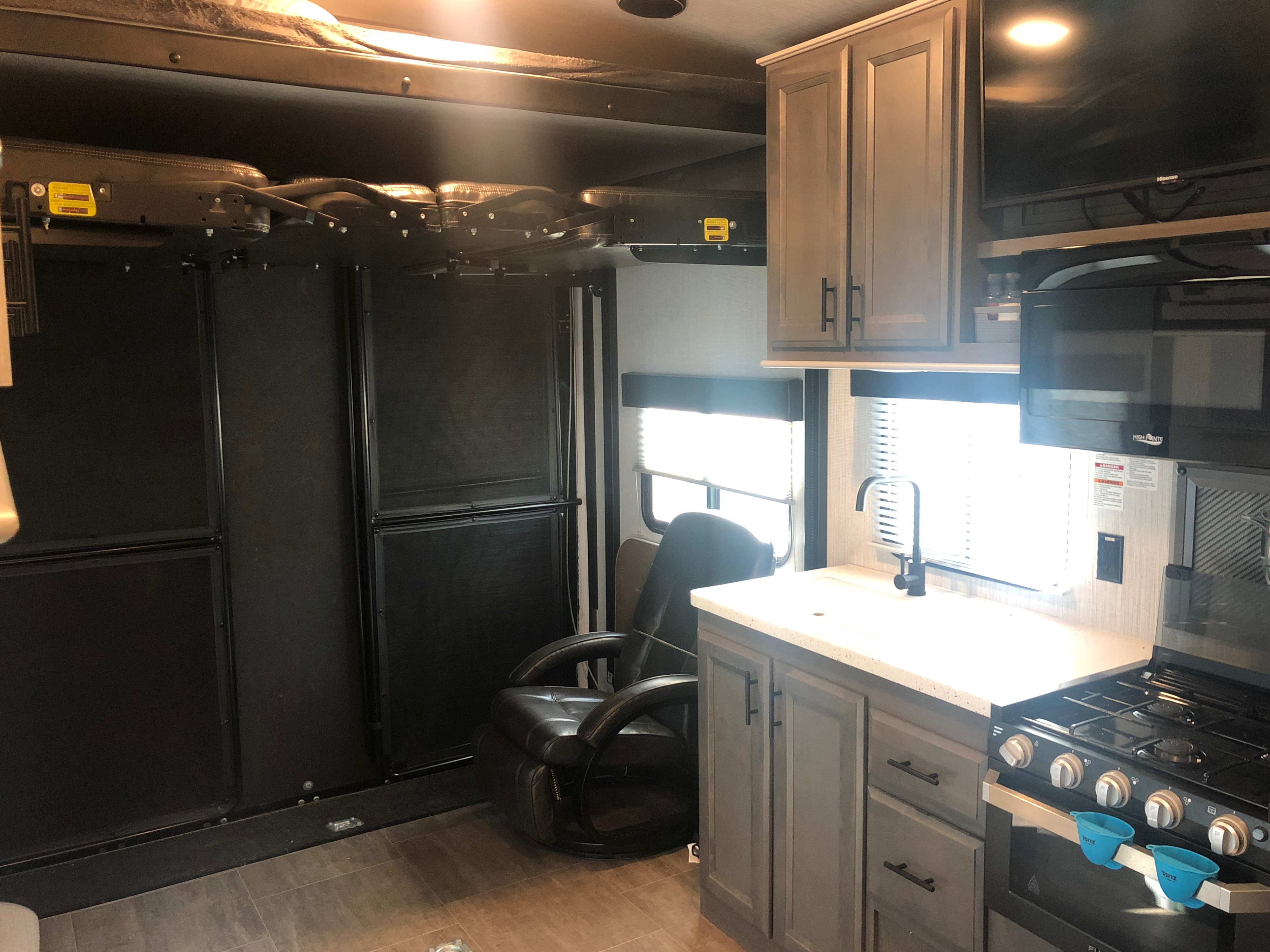 Interior view of an RV rental, showcasing a modern kitchen, recliner chair, and a raised overhead bed for versatile living space.. Cruiser Rv Corp Stryker 2020