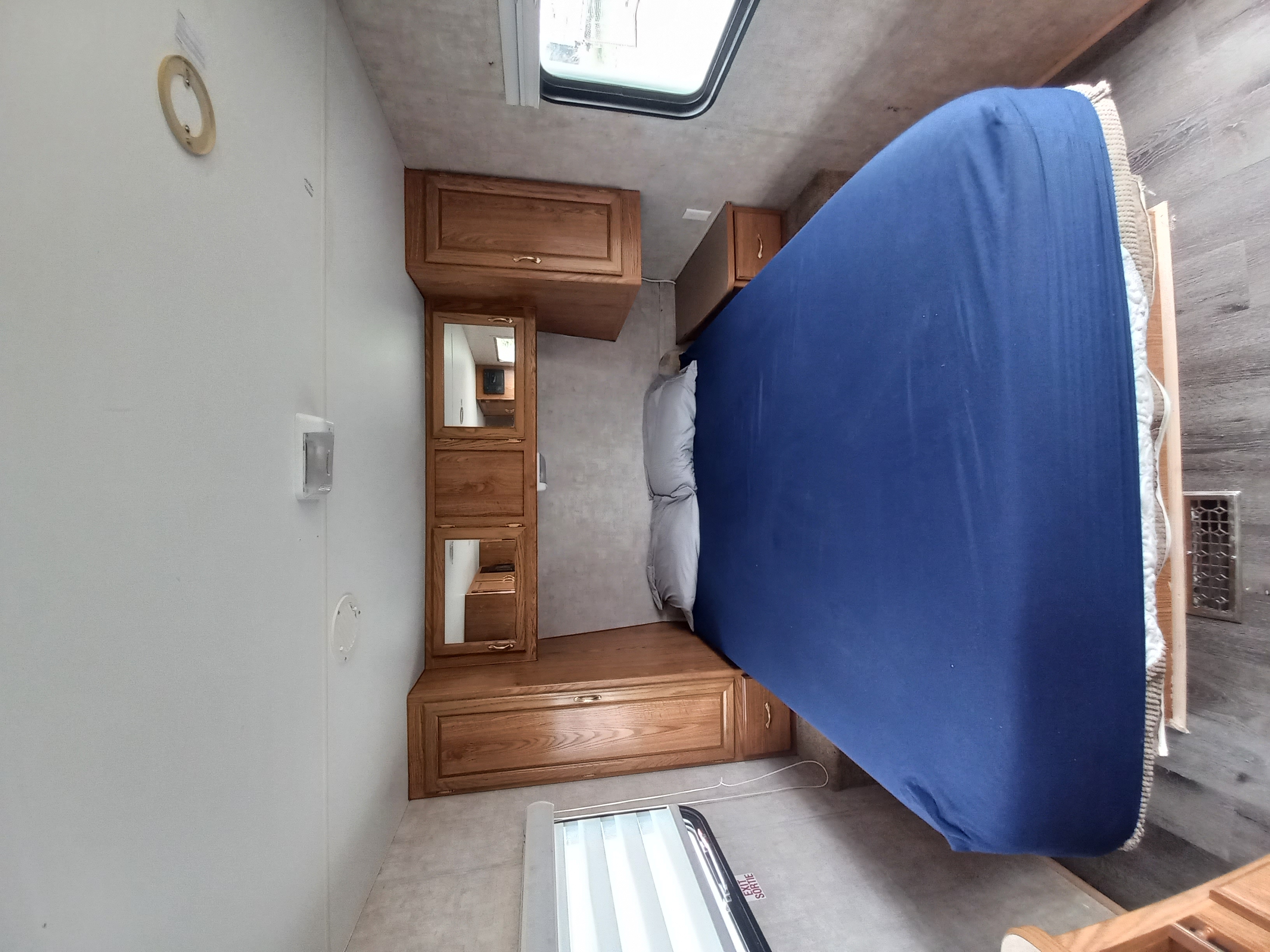 RV rental bedroom: interior view with a blue-sheeted bed, wooden storage cabinets, and an emergency exit window.. Fleetwood 240bh 2005