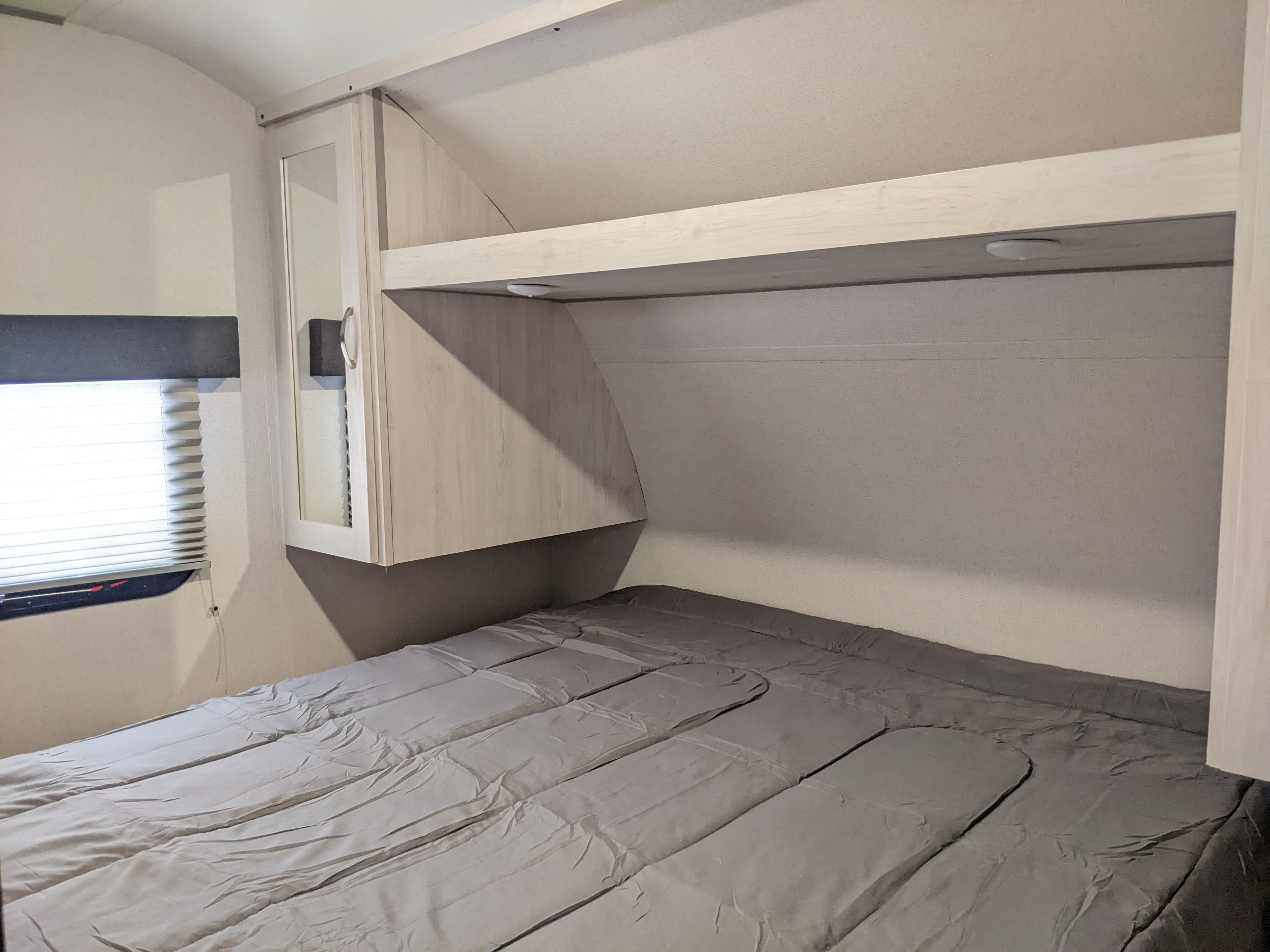 RV rental bedroom. Compact interior featuring a gray bed, built-in shelving, and a window with blinds.. Other Other 2022