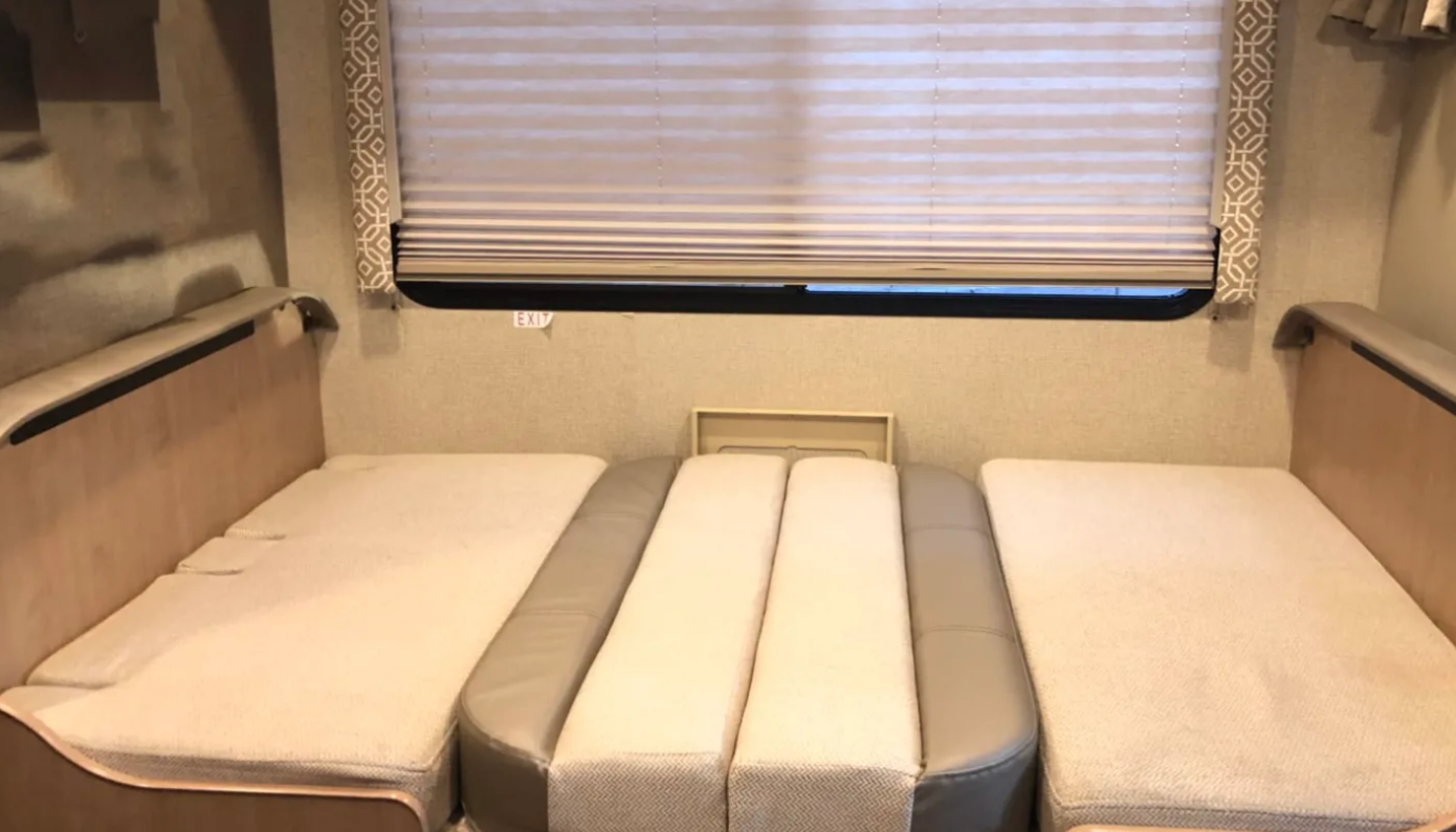 RV rental interior with a convertible dinette bed. Features padded benches, center cushions, and window with blinds.. Thor Motor Coach Chateau 2019