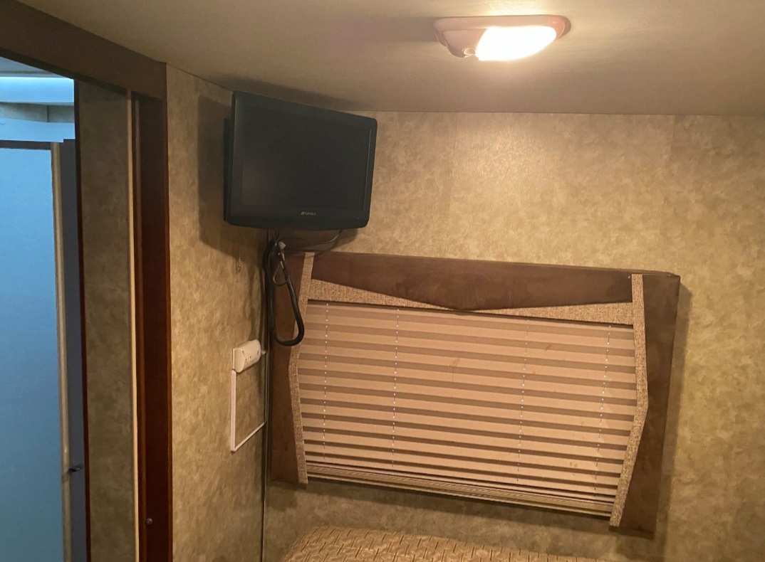 Compact RV rental interior with a wall-mounted TV, window blinds, and bed. Ready for your travels.. Tioga Tioga Motorhome 2012