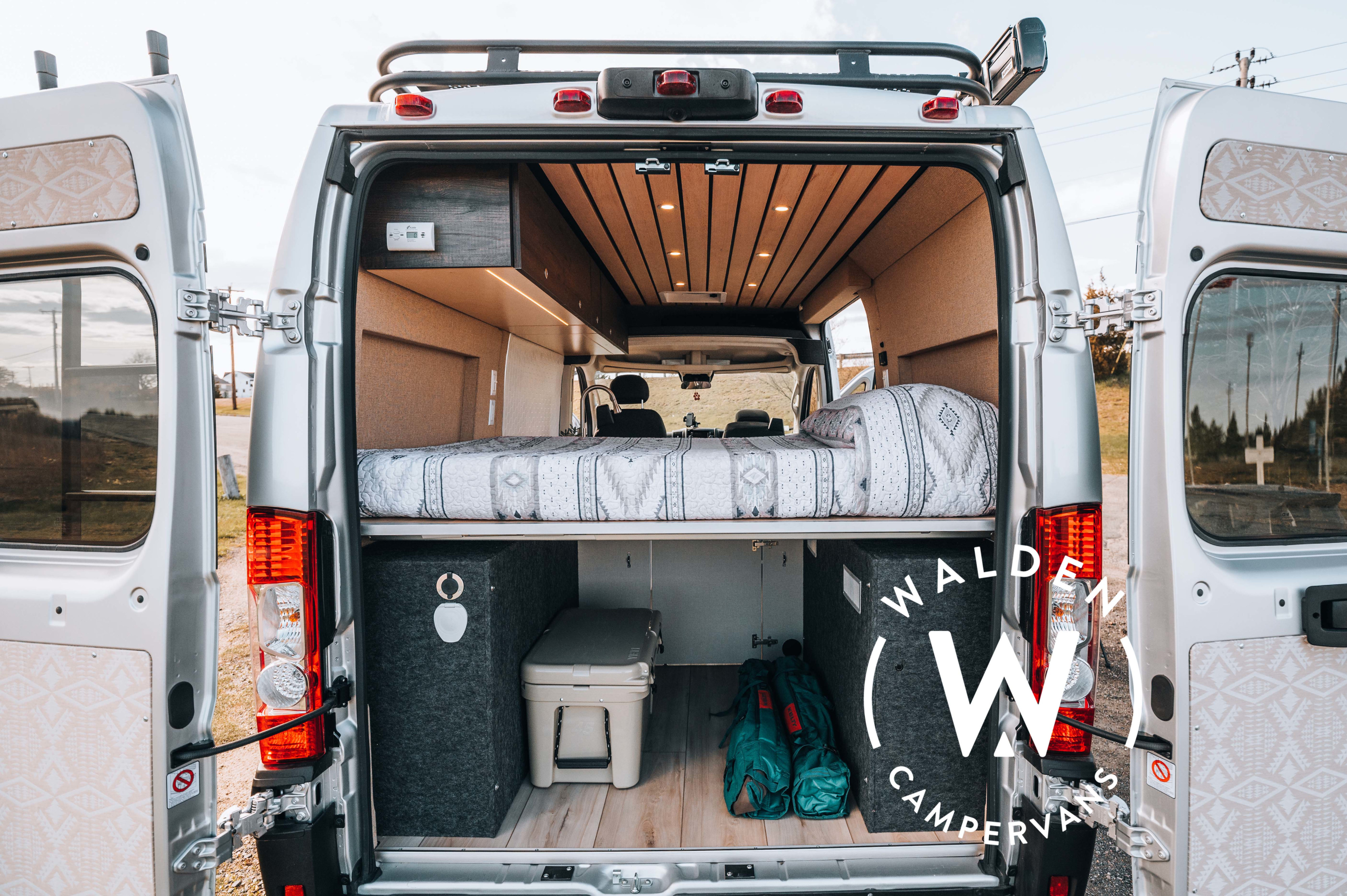Custom RV rental camper van interior: open back doors reveal a comfy bed, wood ceiling, and smart storage for mobile living.. ram Promaster 2021