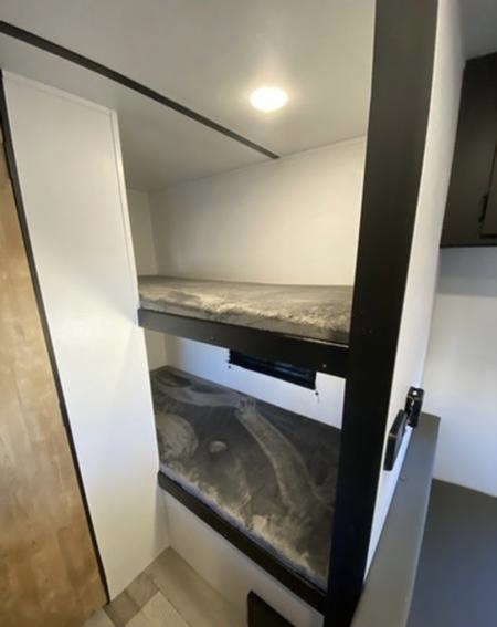 Inside an RV rental: Compact bunk beds with grey blankets, white walls, and an overhead light. Ideal sleeping area.. Keystone Springdale 2022