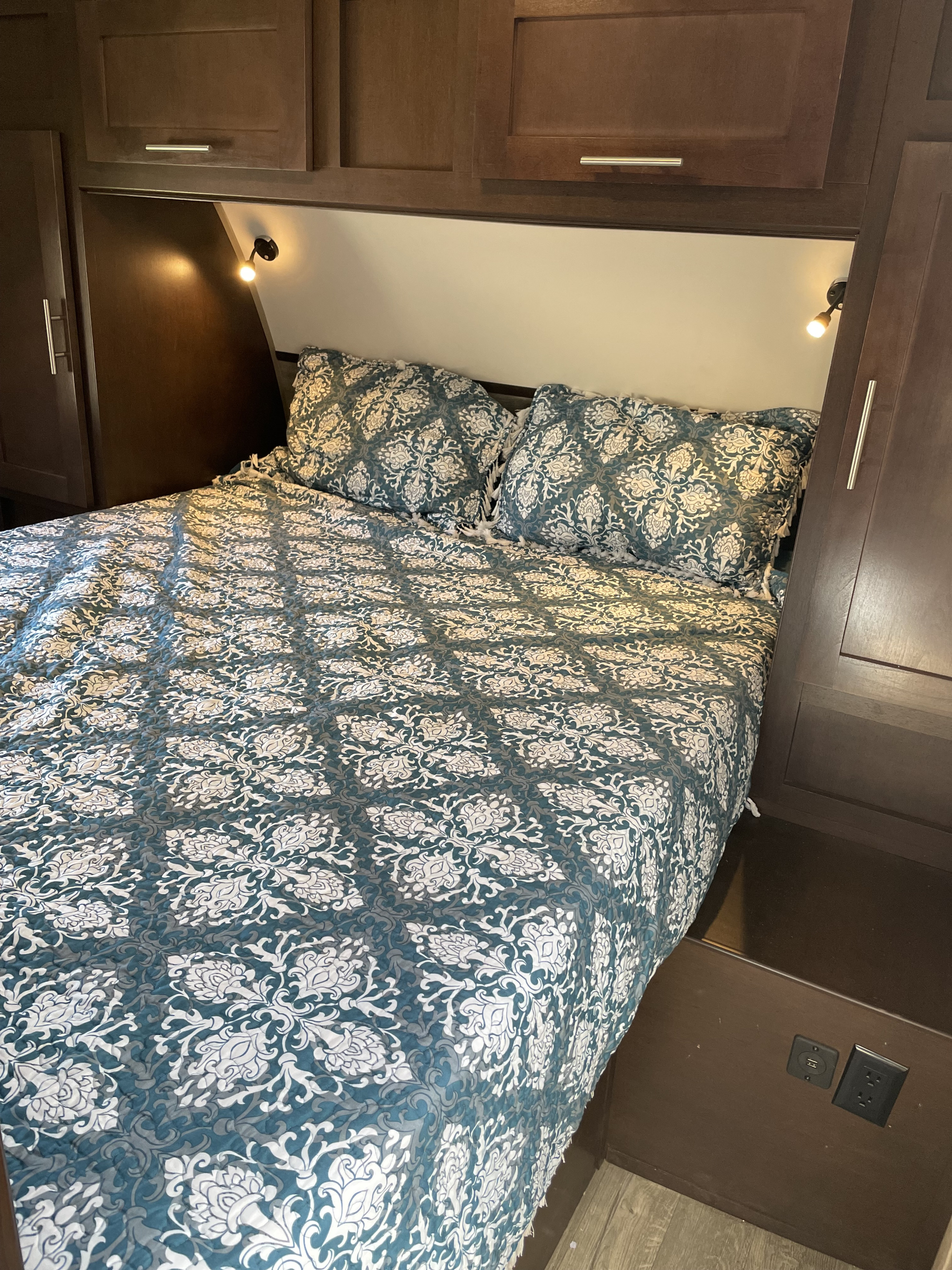 Compact RV rental bedroom featuring patterned bedding, overhead storage, cozy reading lights, and a bedside charging station.. Forest River Cherokee Grey Wolf 2017