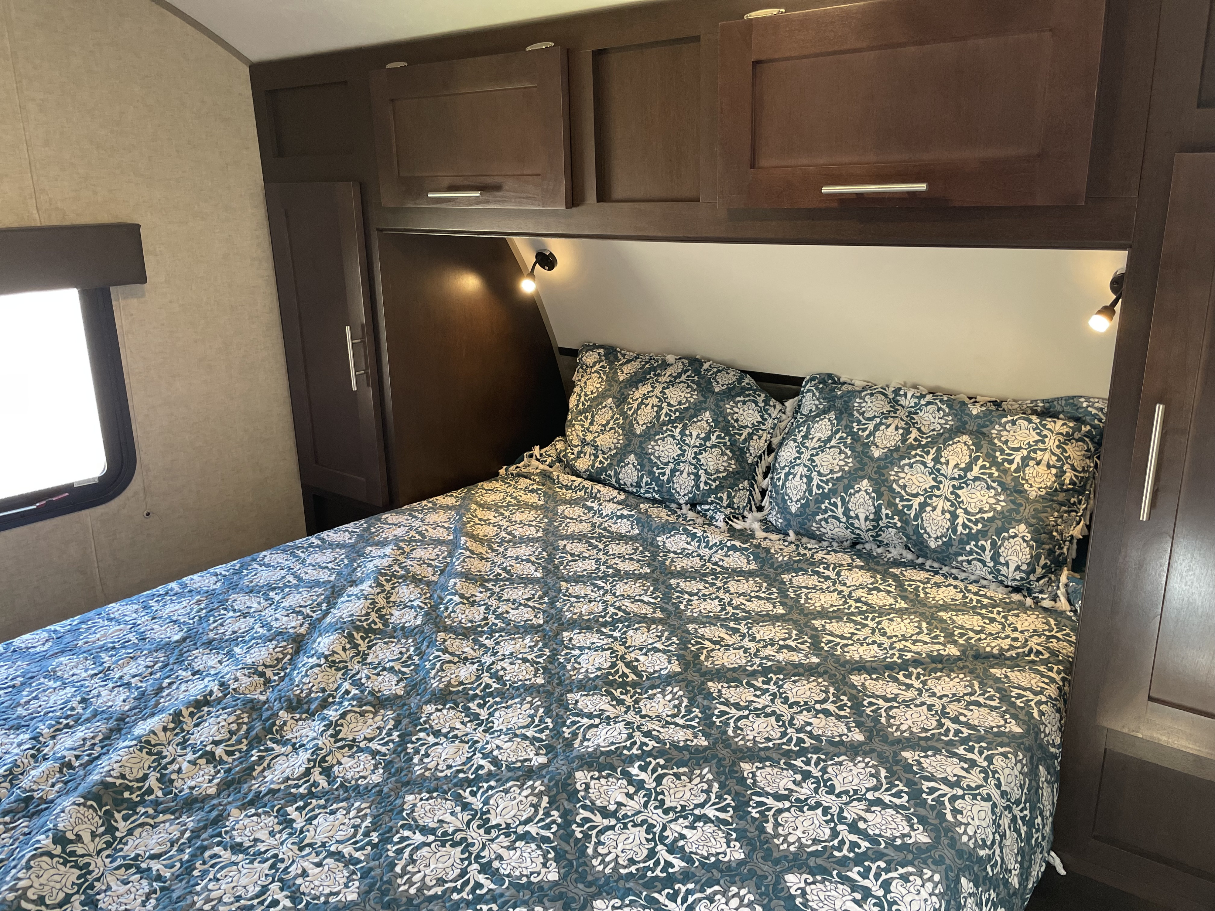 Cozy RV rental bedroom with patterned bedspread, overhead cabinets, and reading lights, perfect for comfortable travel.. Forest River Cherokee Grey Wolf 2017