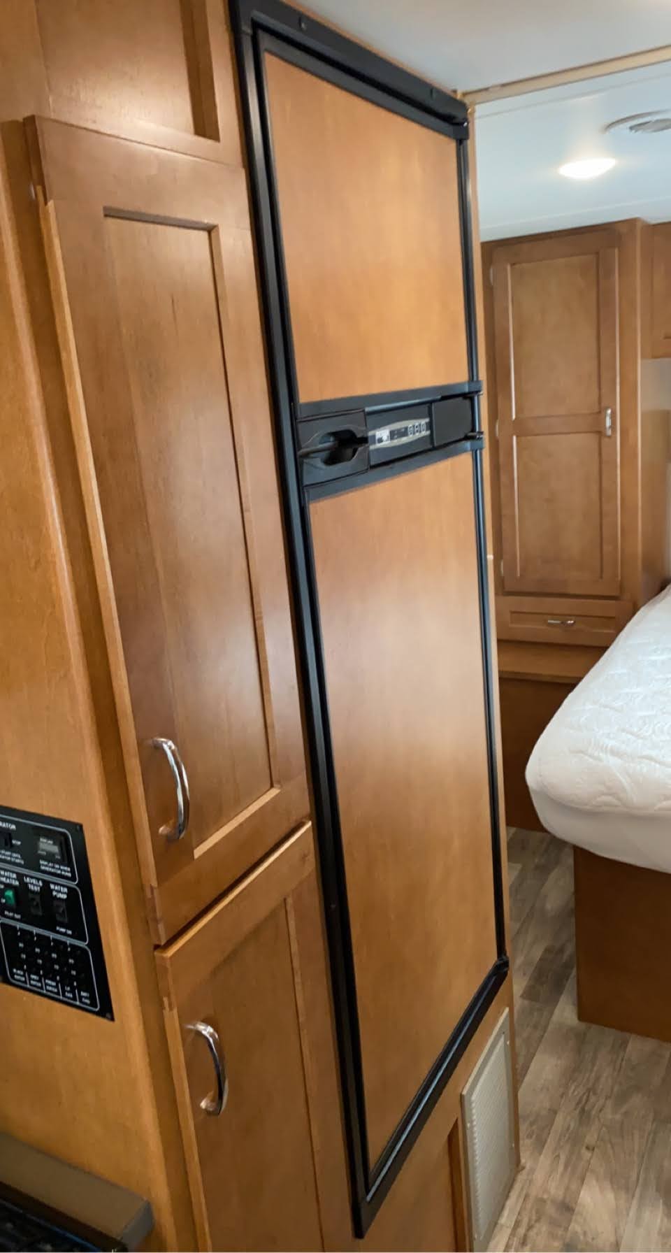 An RV rental interior showing a wood-paneled refrigerator, storage cabinets, and a control panel.. Winnebago Minnie Winnie 2017