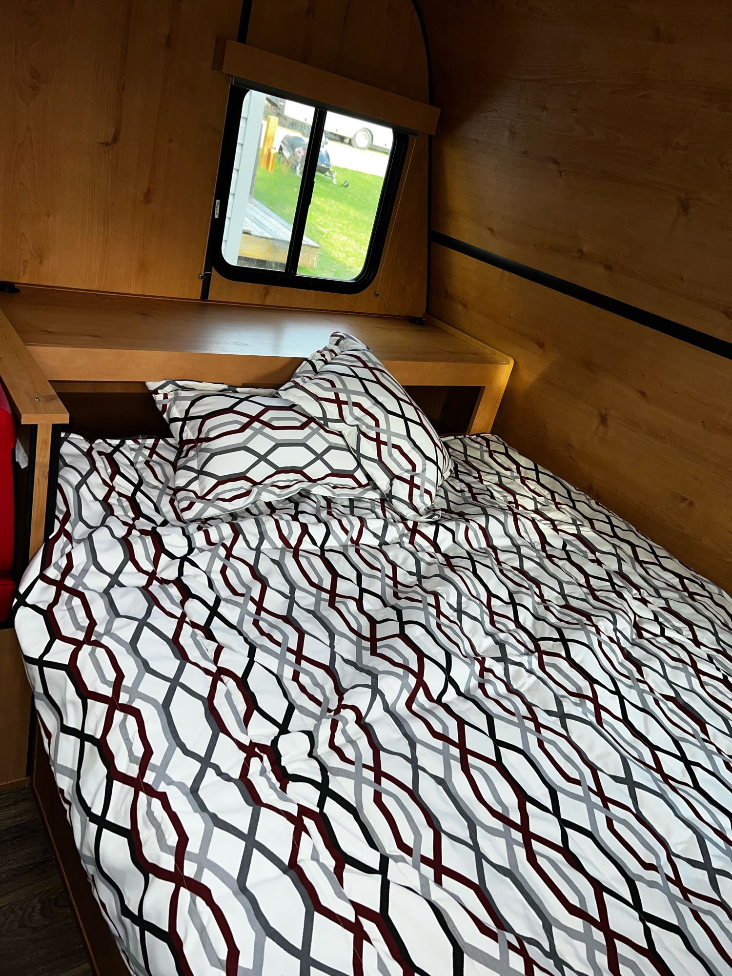 Cozy rv rental bed area: wood-paneled interior, geometric bedding, and window overlooking a yard.. Old School Trailers 821 2022