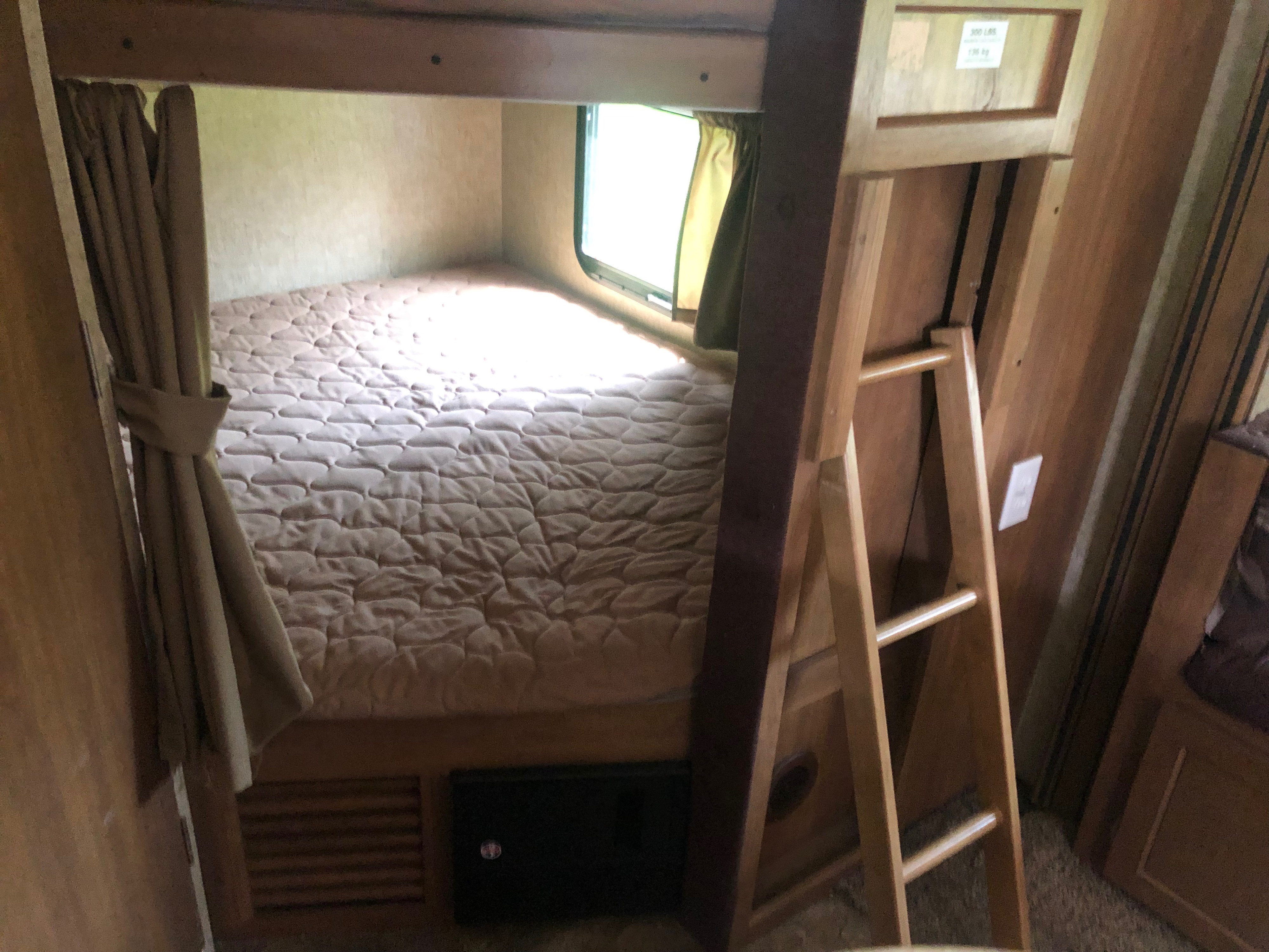 Inside an RV rental: a cozy lower bunk bed with quilted mattress, window with curtains, and a wooden ladder.. Coachmen Apex 2016