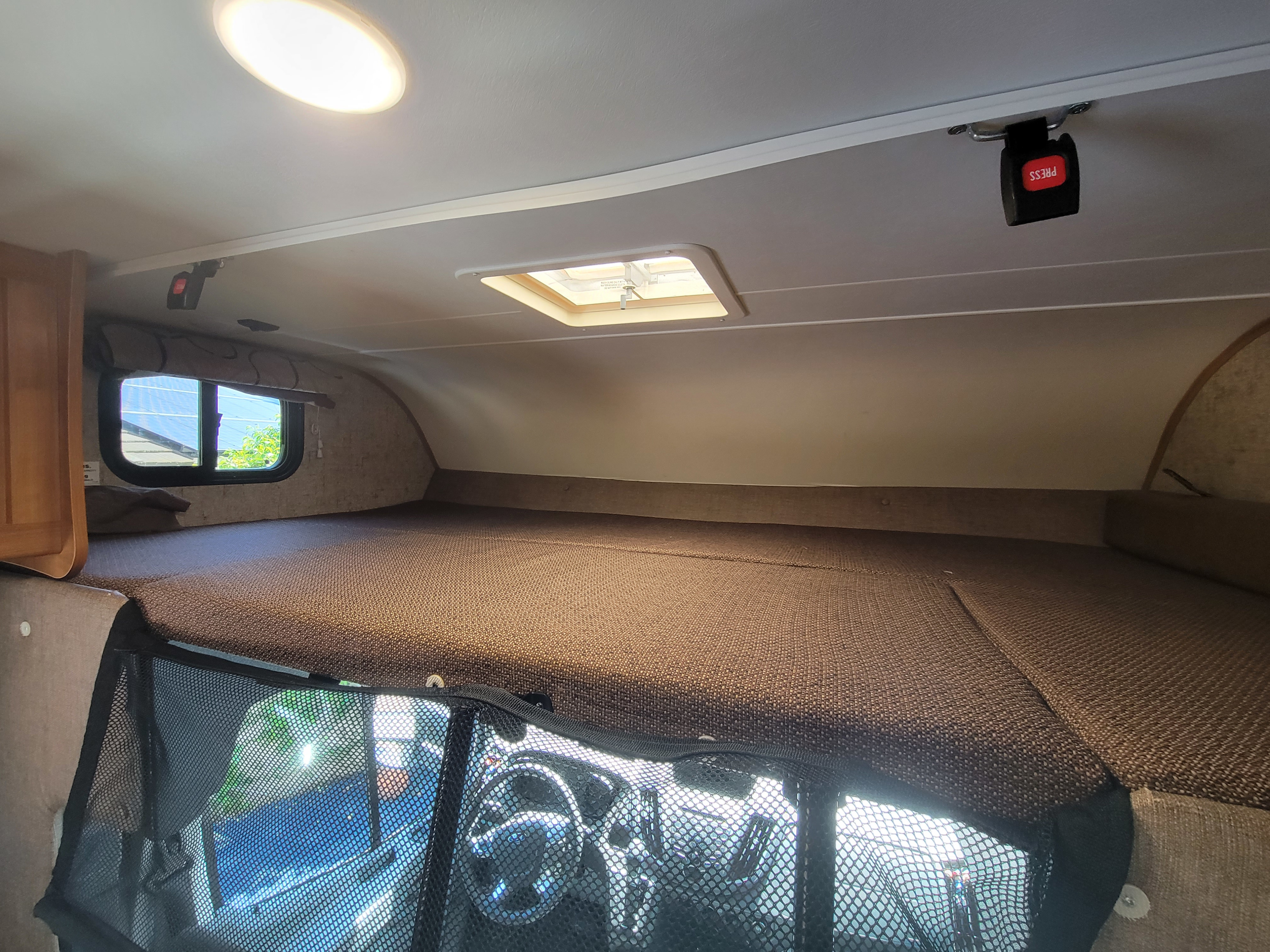 Cozy cab-over bunk in an RV rental, featuring a spacious sleeping area, window, light, vent, and safety mesh.. Coachman Leprechaun 2018