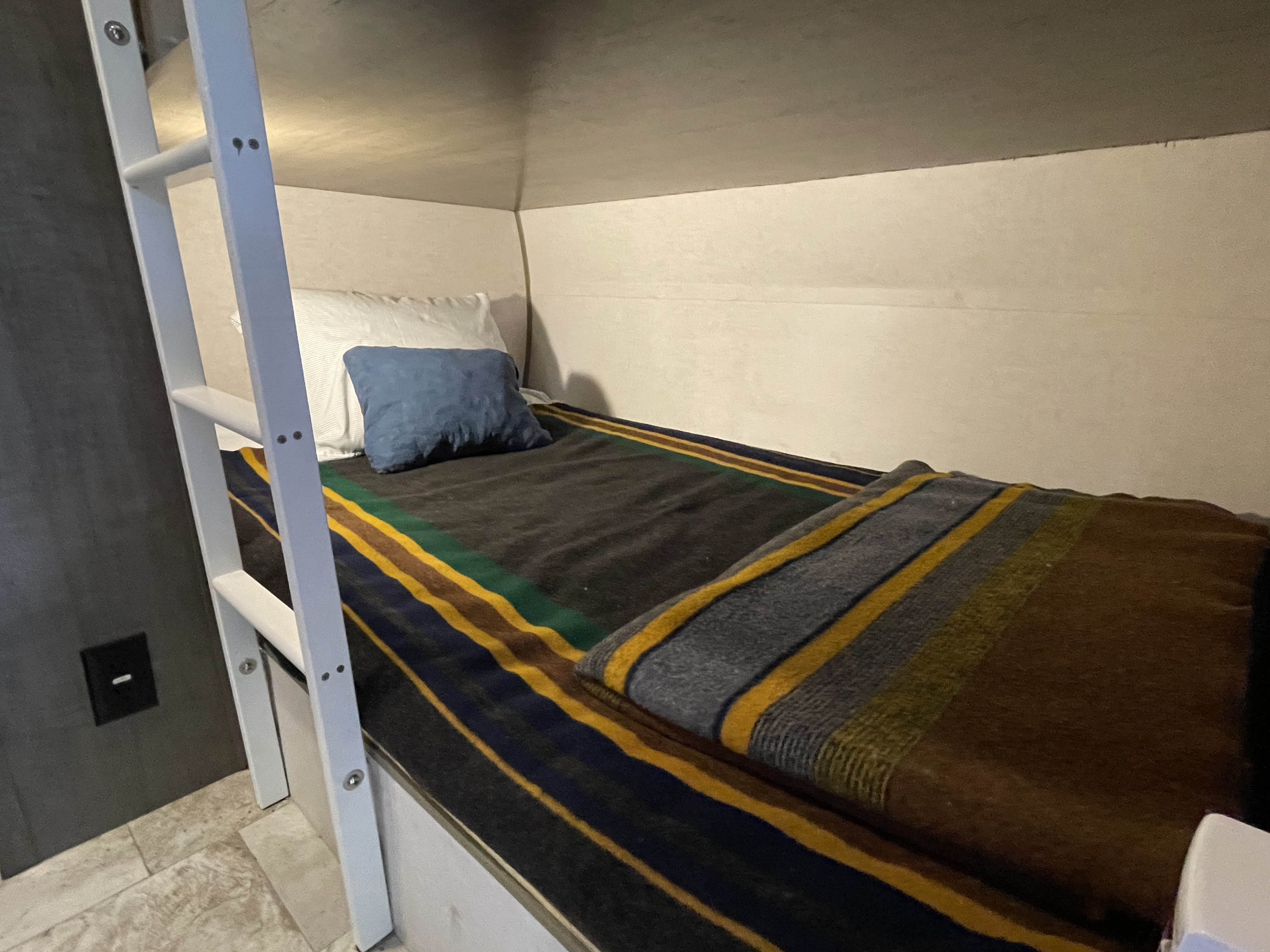 Cozy RV rental bunk bed with a striped blanket, white pillow, and blue accent pillow, accessed by a white ladder.. R-Pod Hood River Edition 2017