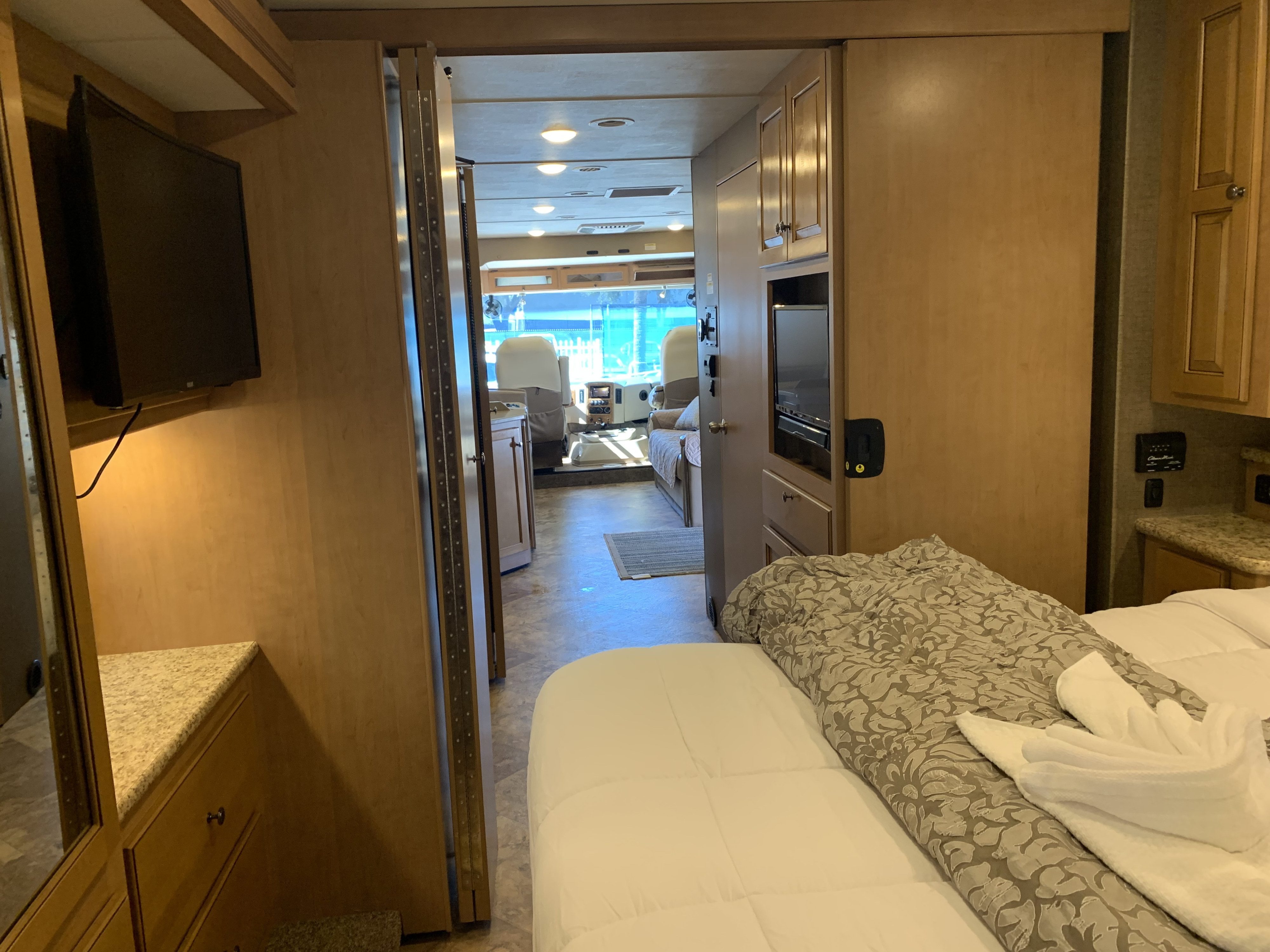 RV rental bedroom and living space interior. A bed, TVs, and front cockpit are visible, providing a full view of the RV's layout.. Thor Windsport 2017