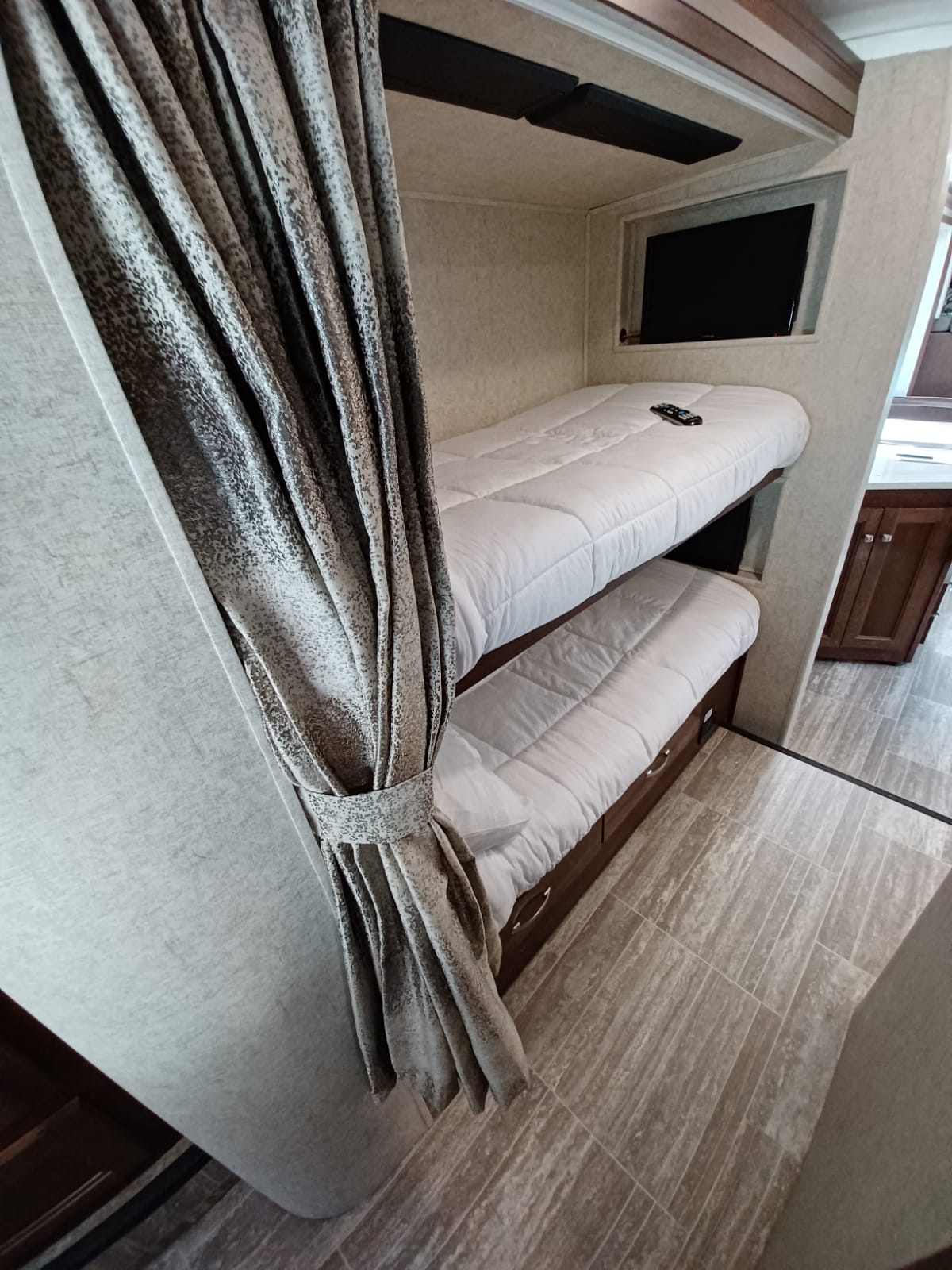 Inside an RV rental: a pair of cozy bunk beds with white bedding, a wall-mounted TV, and a decorative privacy curtain.. Forest River Forester 2020