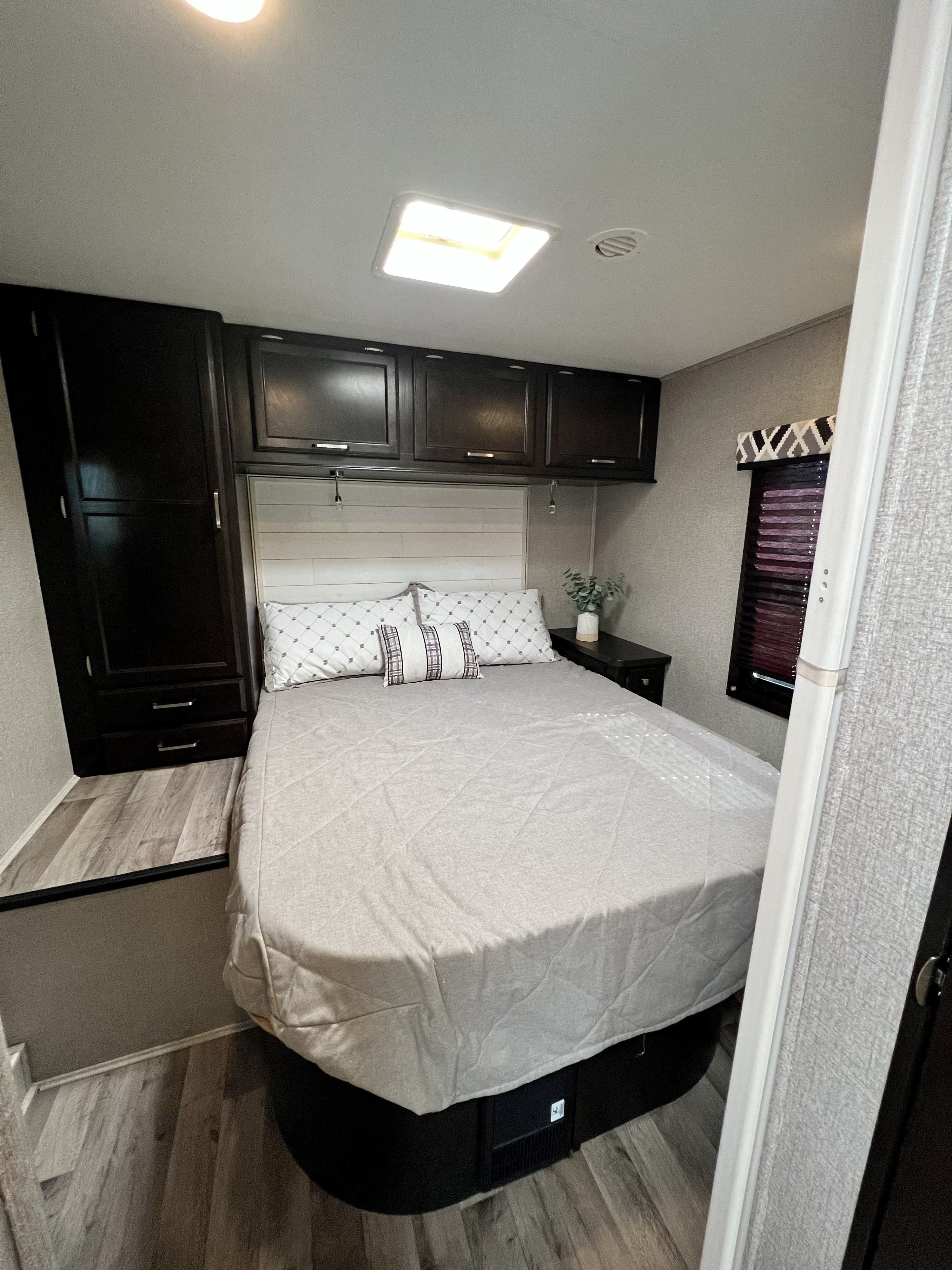 Cozy RV rental bedroom featuring a comfortable bed, dark wood cabinetry, window, and overhead skylight.. Entegra Coach Odyssey 2021