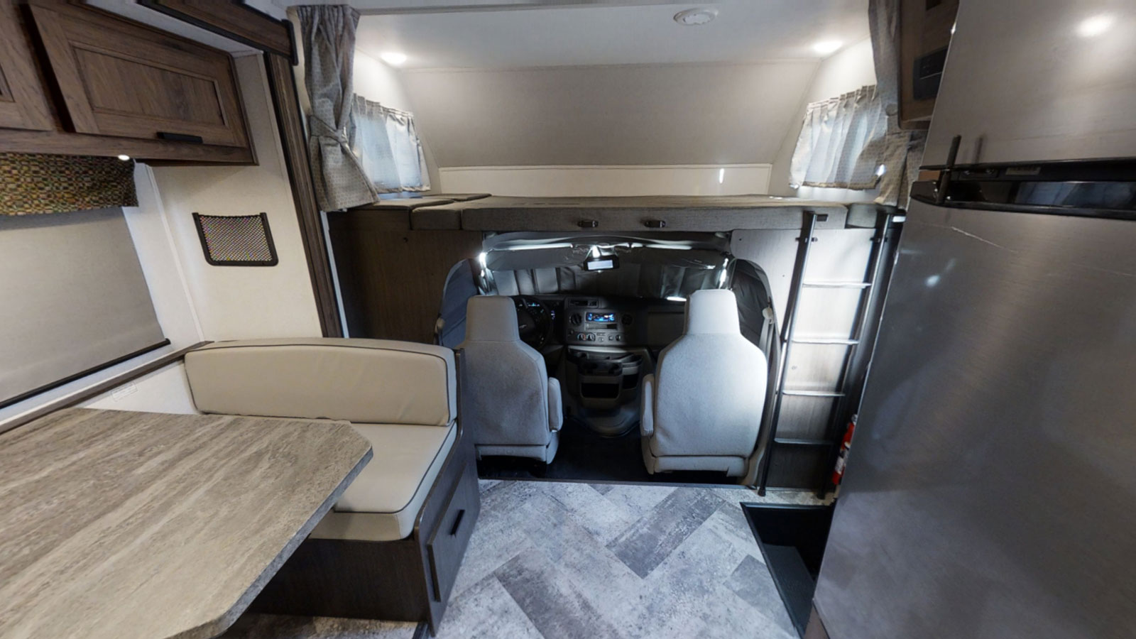 RV rental interior: view of dinette, over-cab bunk, driver's area, and a large refrigerator.. Forest River 2550DSLE 2022