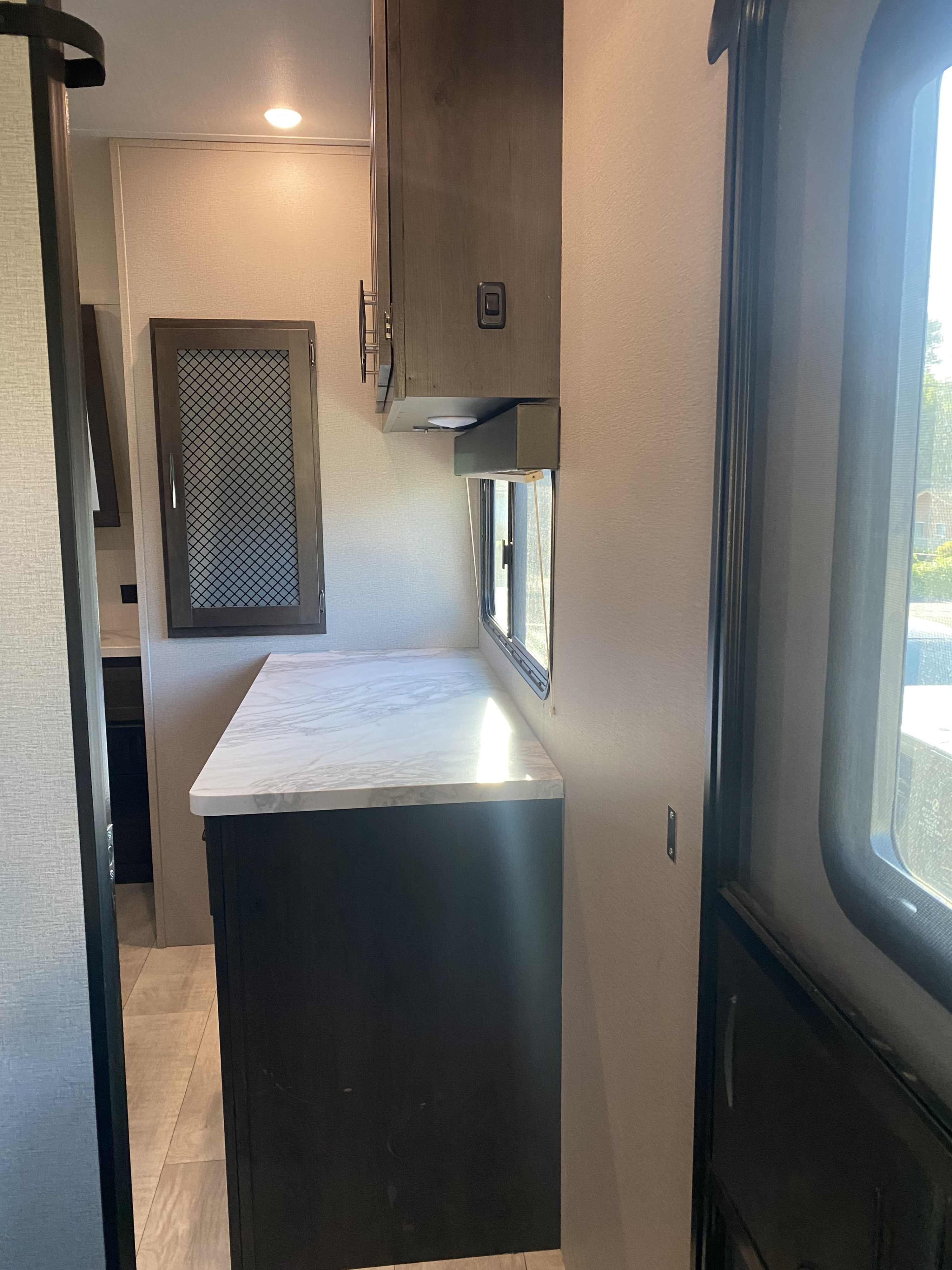 Bright rv rental interior featuring a modern kitchen counter, overhead cabinets, and a window for natural light.. Grand Design Momentum 2021