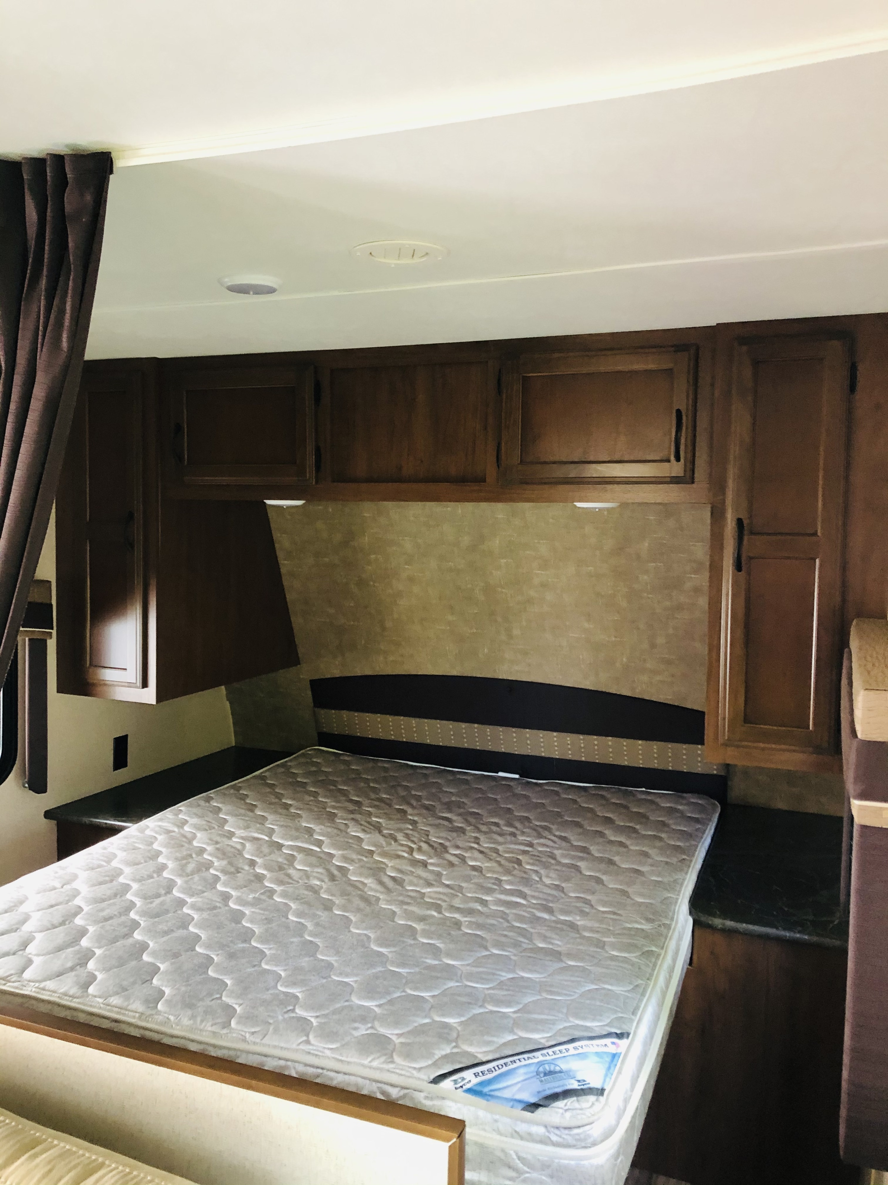View of a compact bedroom in an RV rental, featuring a bed, dark wood cabinets, and a textured headboard.. Jayco Jay Flight 2016