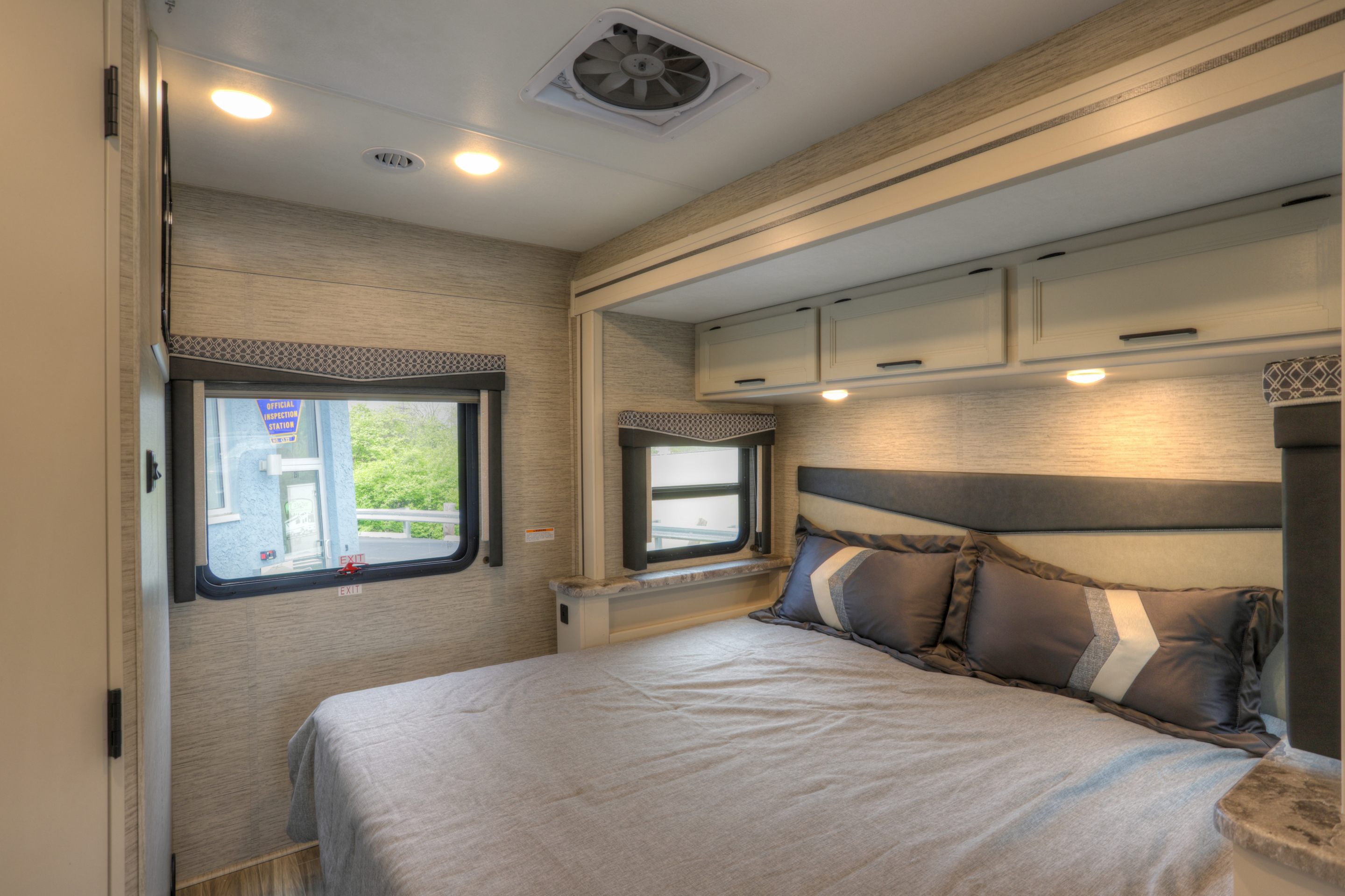 Bright RV rental bedroom: comfortable bed, ample overhead storage, windows, and ceiling fan for travel comfort.. Thor Motor Coach A.C.E 2022