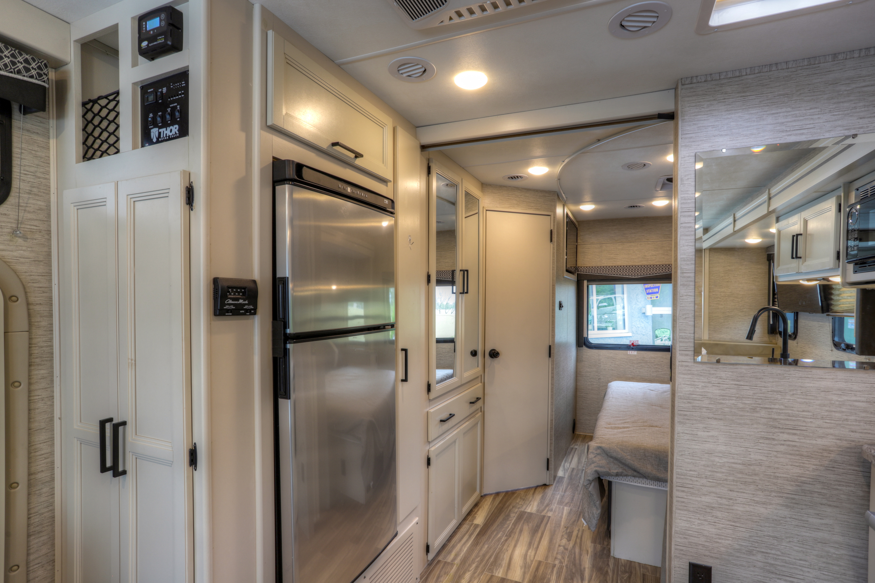Modern RV rental interior, featuring a stainless steel refrigerator, control panel, compact kitchen with a mirror, and cozy bedroom.. Thor Motor Coach A.C.E 2022