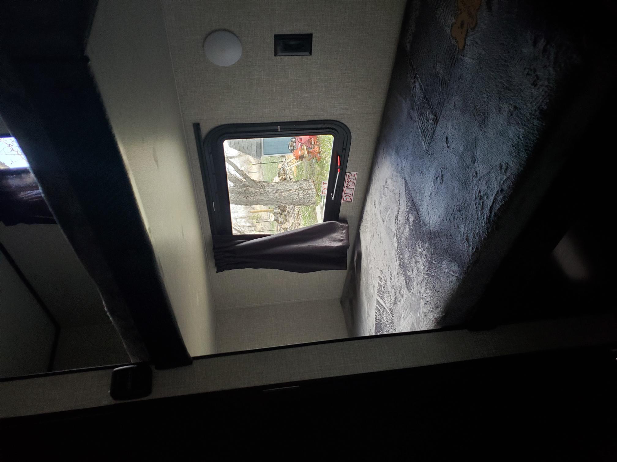 A cozy rv rental bunk bed area, showing an upper and lower bunk. A window with an 'EXIT SORTIE' sticker offers a view of trees.. Jayco Jay Flight SLX Baja 2022