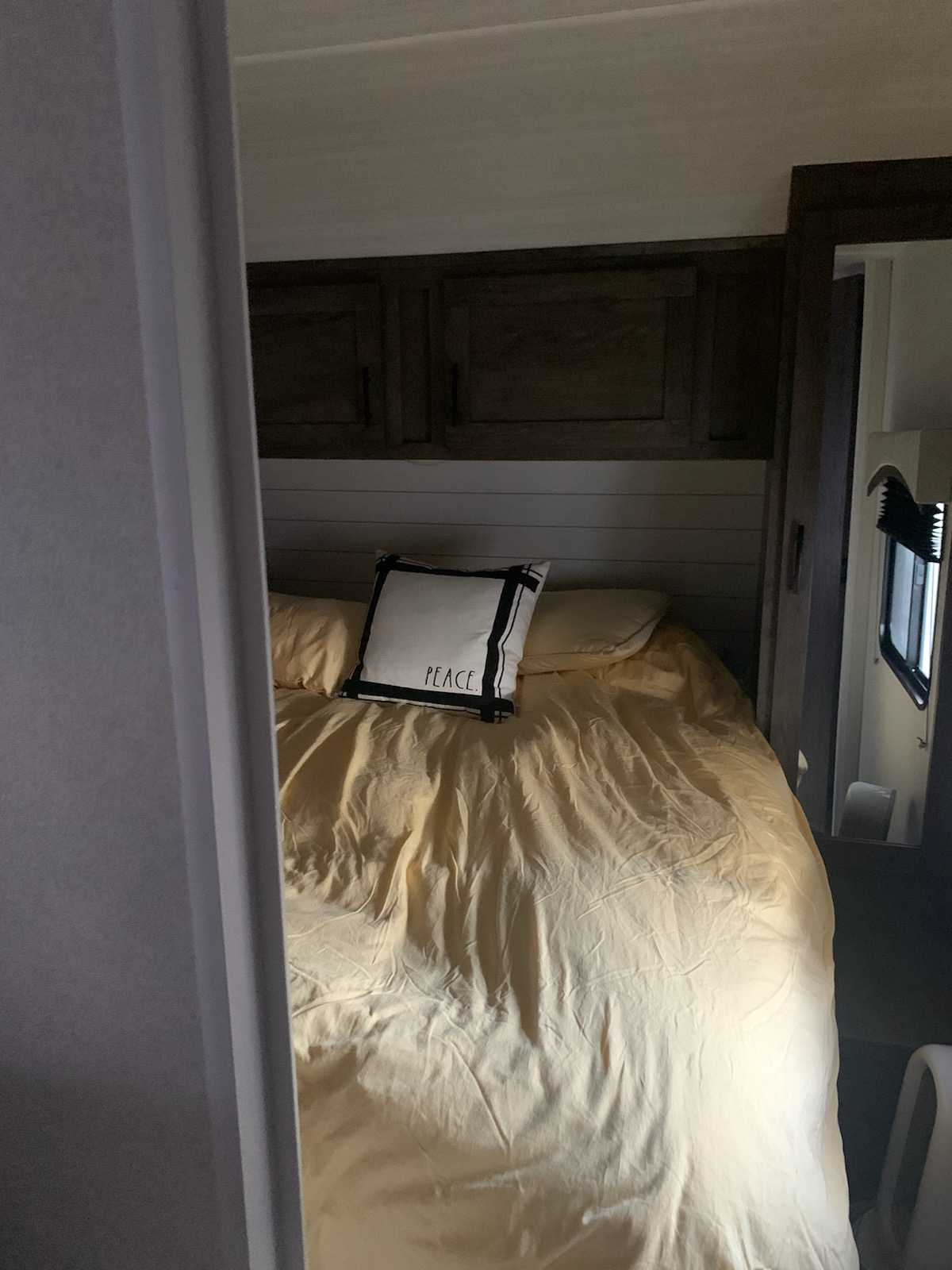 Inside an RV rental: a cozy bedroom with yellow bedding, a "PEACE" pillow, and storage cabinets above the bed.. Forest River EVO 3250 2021