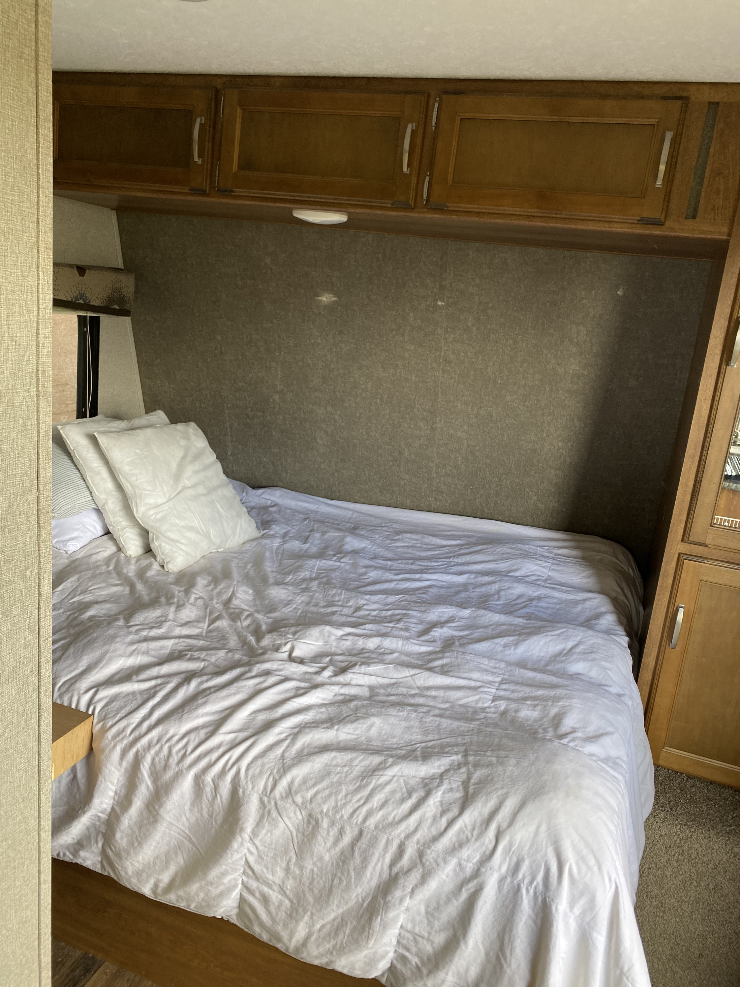 Compact RV rental bedroom featuring a bed with white linen, pillows, and wooden overhead cabinets.. Keystone RV Springdale 2017