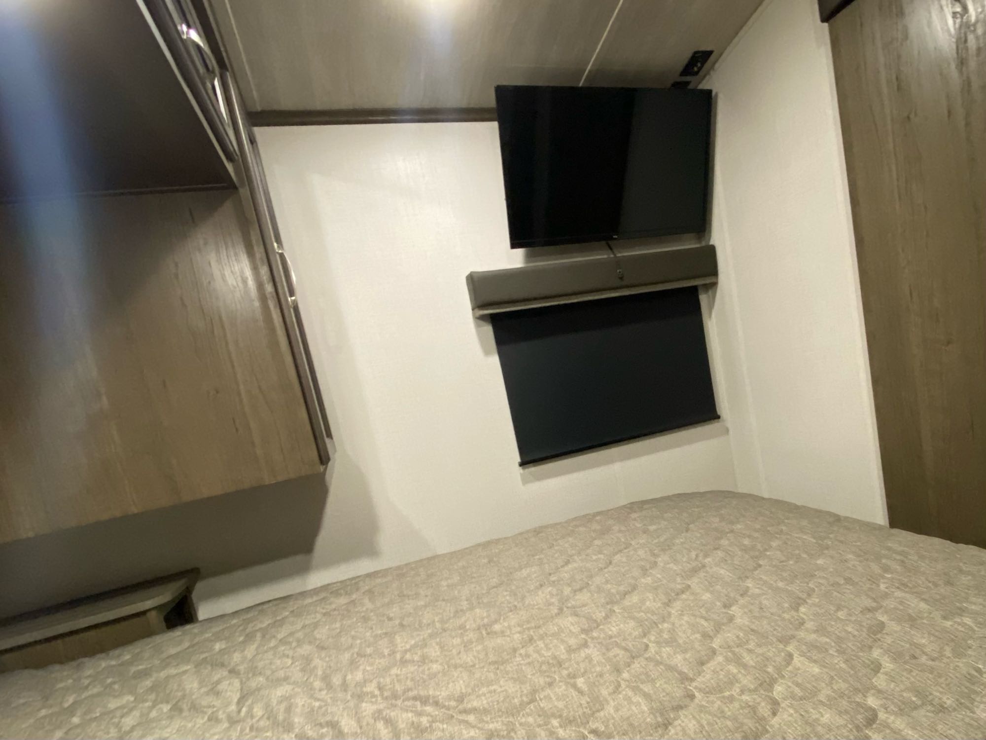 Inside a cozy **rv rental** bedroom, featuring a mounted TV, soundbar, and a drawn window blind above a comfortable bed.. Keystone Cougar 25DBSWE 2022
