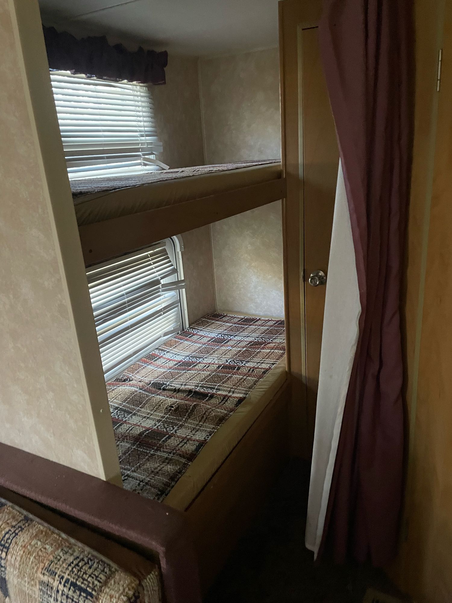 Two bunk beds with plaid and plain covers, blinds on windows, and a curtained doorway inside an RV rental.. Dutchmen Sport 2004