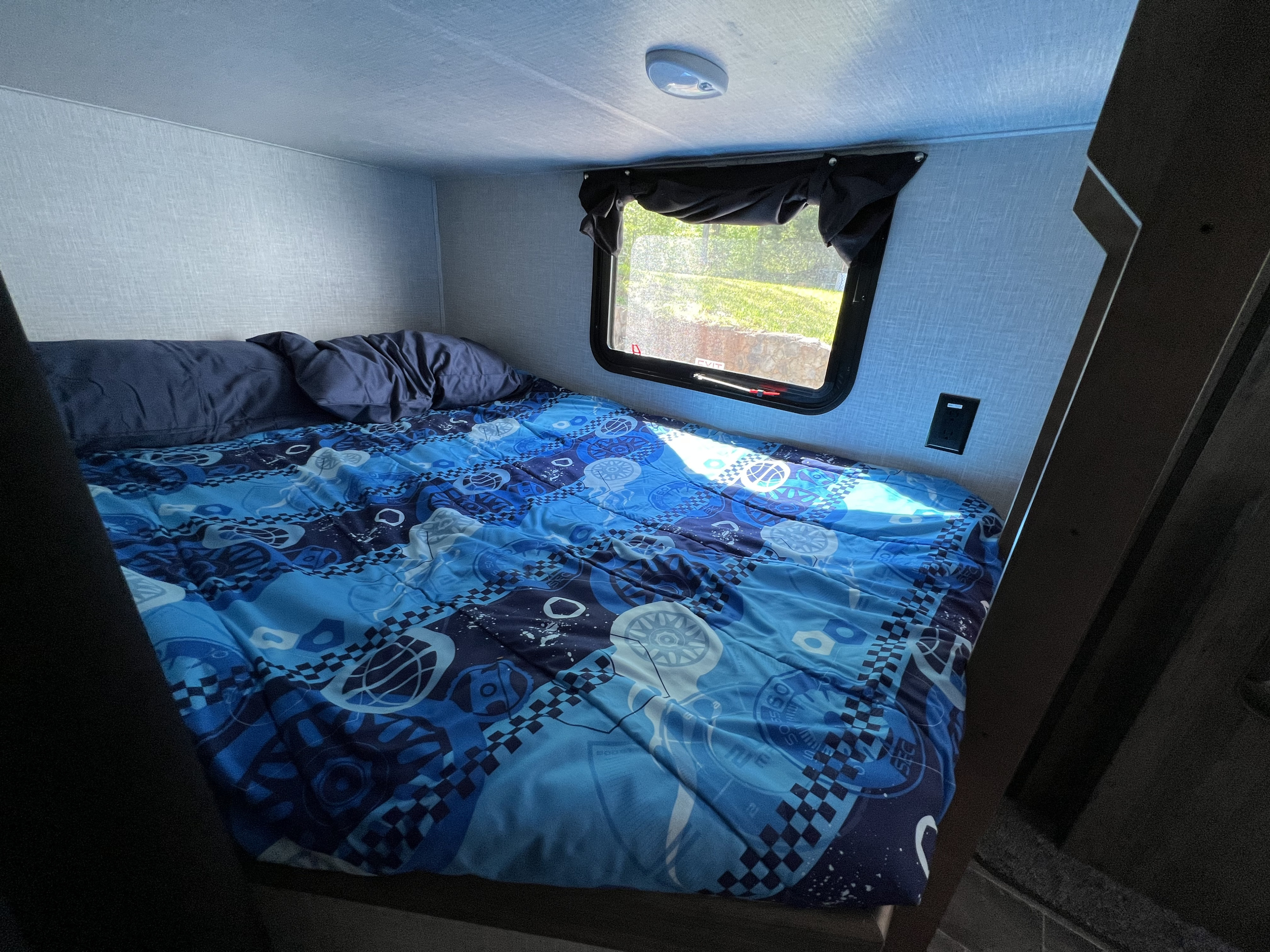 Inside an RV rental, a comfy bunk bed with a blue patterned comforter and natural light from the window.. Crossroads 270BH 2022