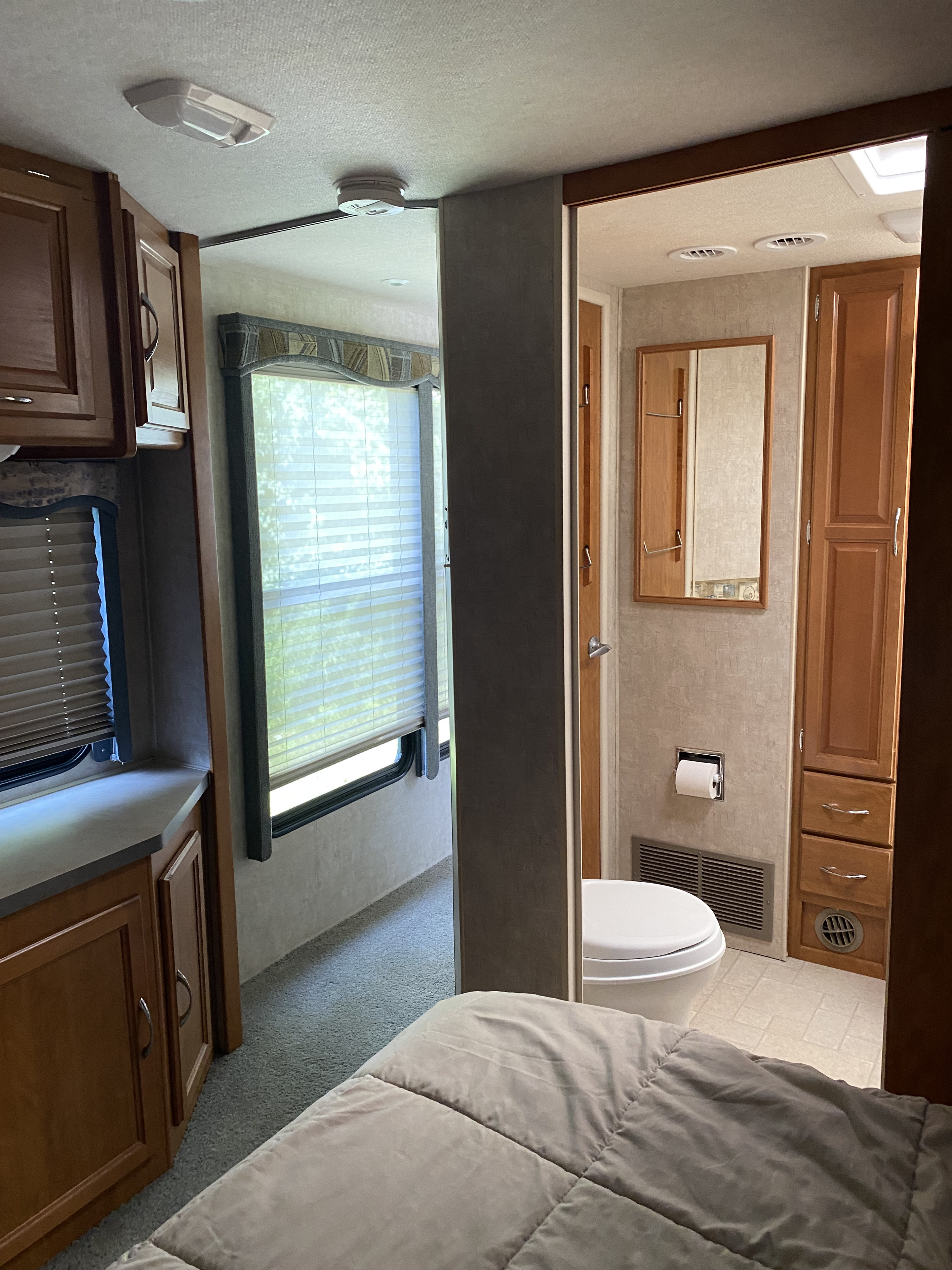 Inside an RV rental: view from the bedroom to a compact bathroom & living area, featuring windows, blinds, and cabinetry.. Fleetwood Jamboree 2005