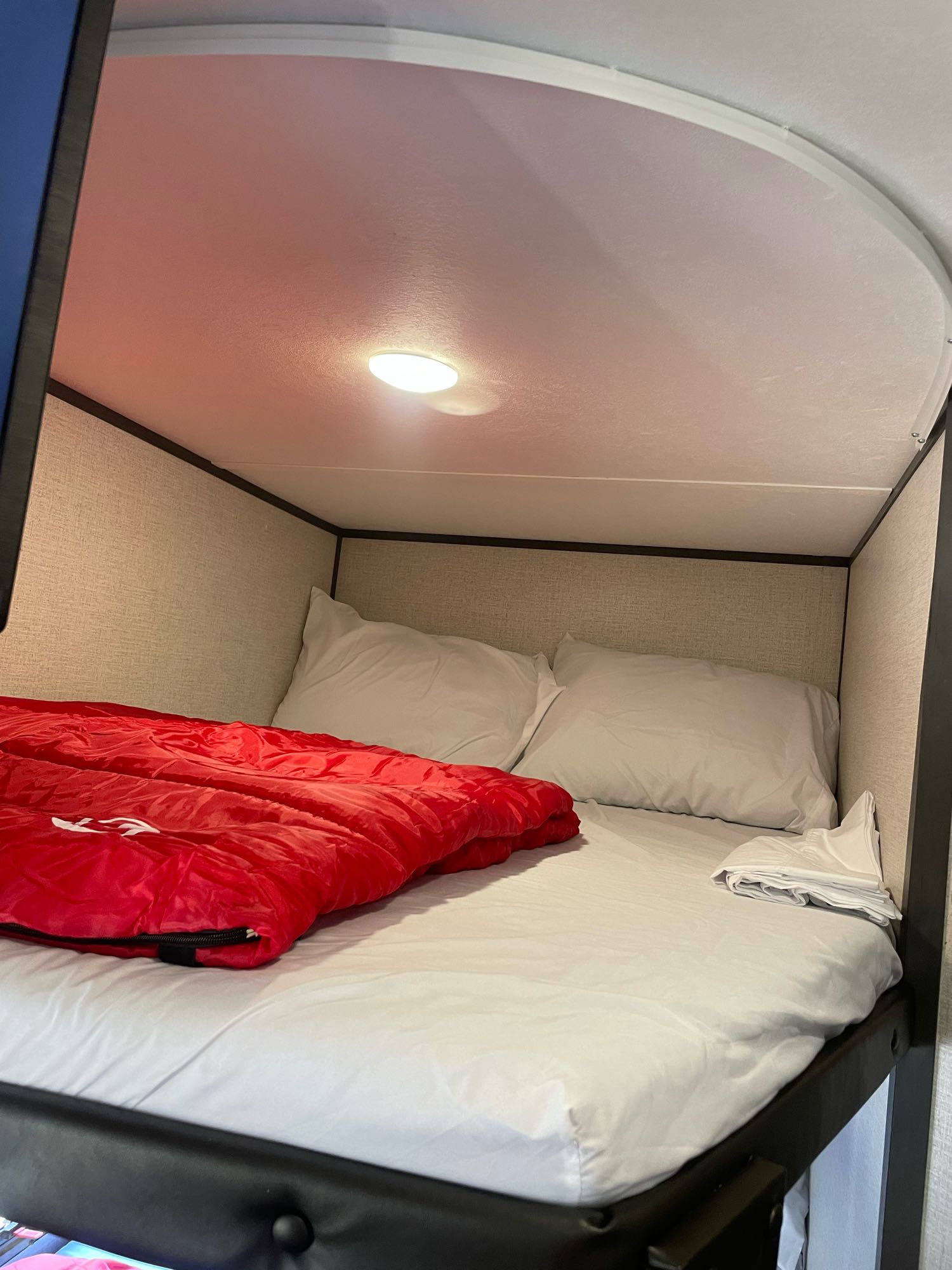 Inside an RV rental: a neat bunk bed with white sheets, pillows, and a vibrant red sleeping bag.. Aspen Trail 25 BH 2022