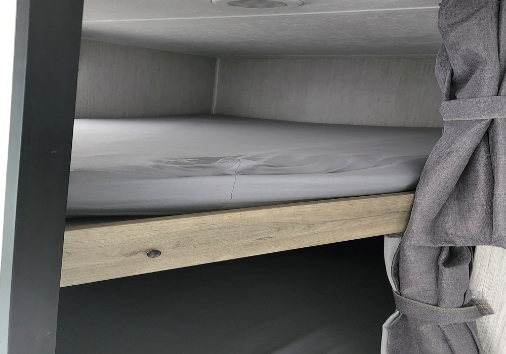 Inside an RV rental: a neat bunk bed with grey sheets and a tied-back privacy curtain, ready for cozy nights.. Forest River Puma 2021