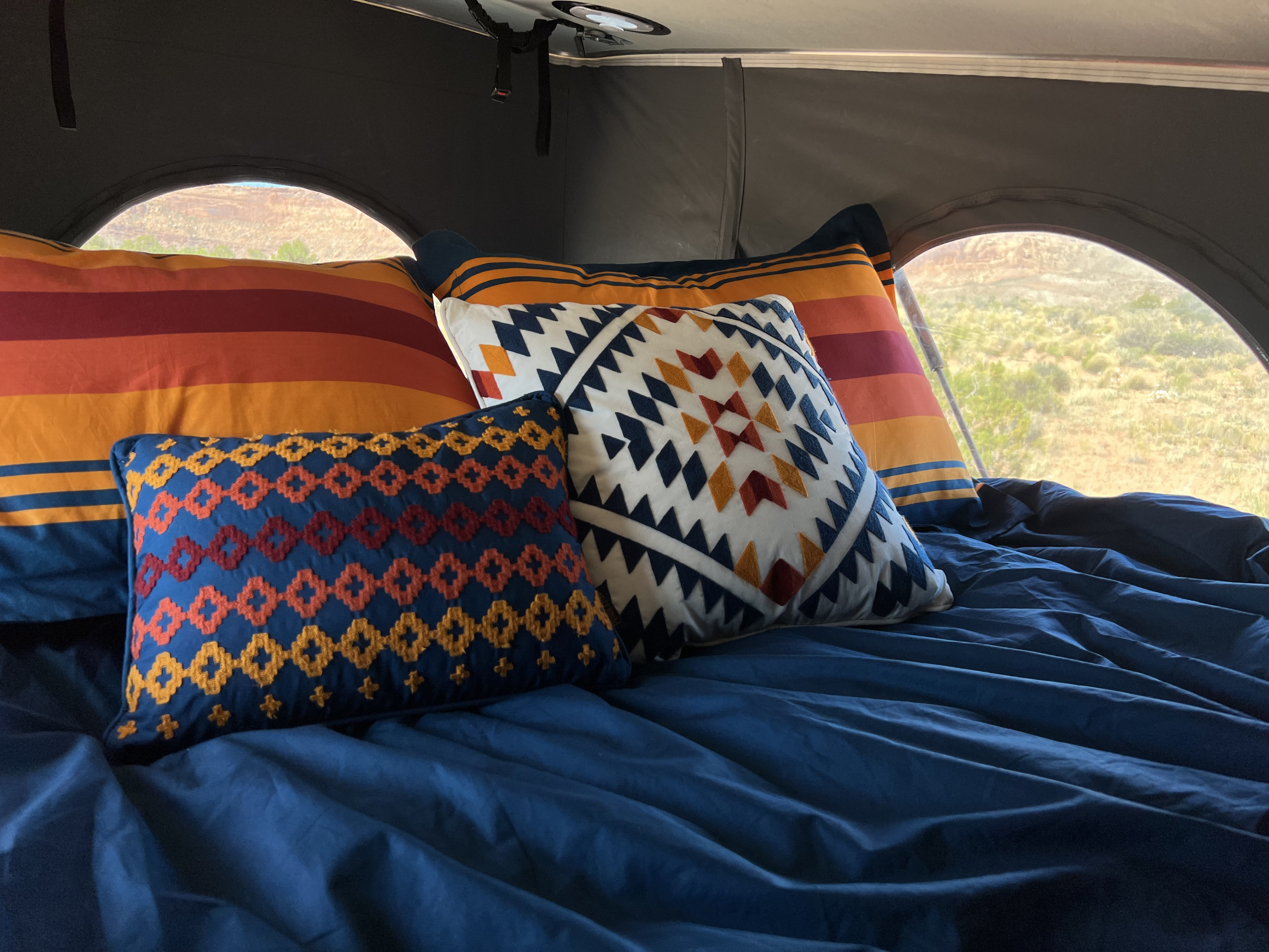 Cozy bed in an RV rental, featuring vibrant southwestern pillows, blue sheets, and a serene desert view.. Winnebago Solis 2022