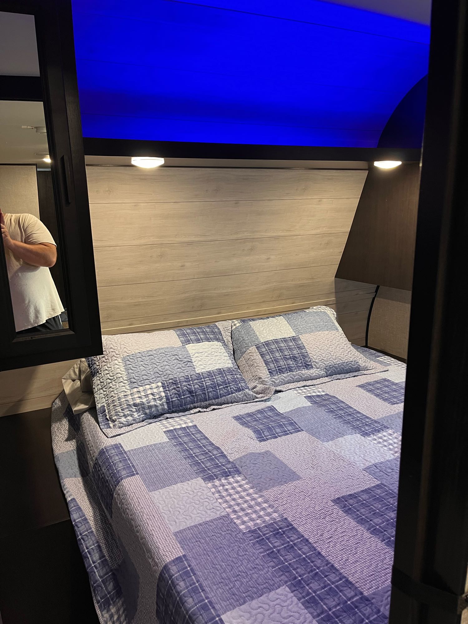 Cozy RV rental bedroom featuring a comfortable bed with a patchwork quilt, blue LED lighting, and a person in reflection.. Jayco Jay Flight 2022