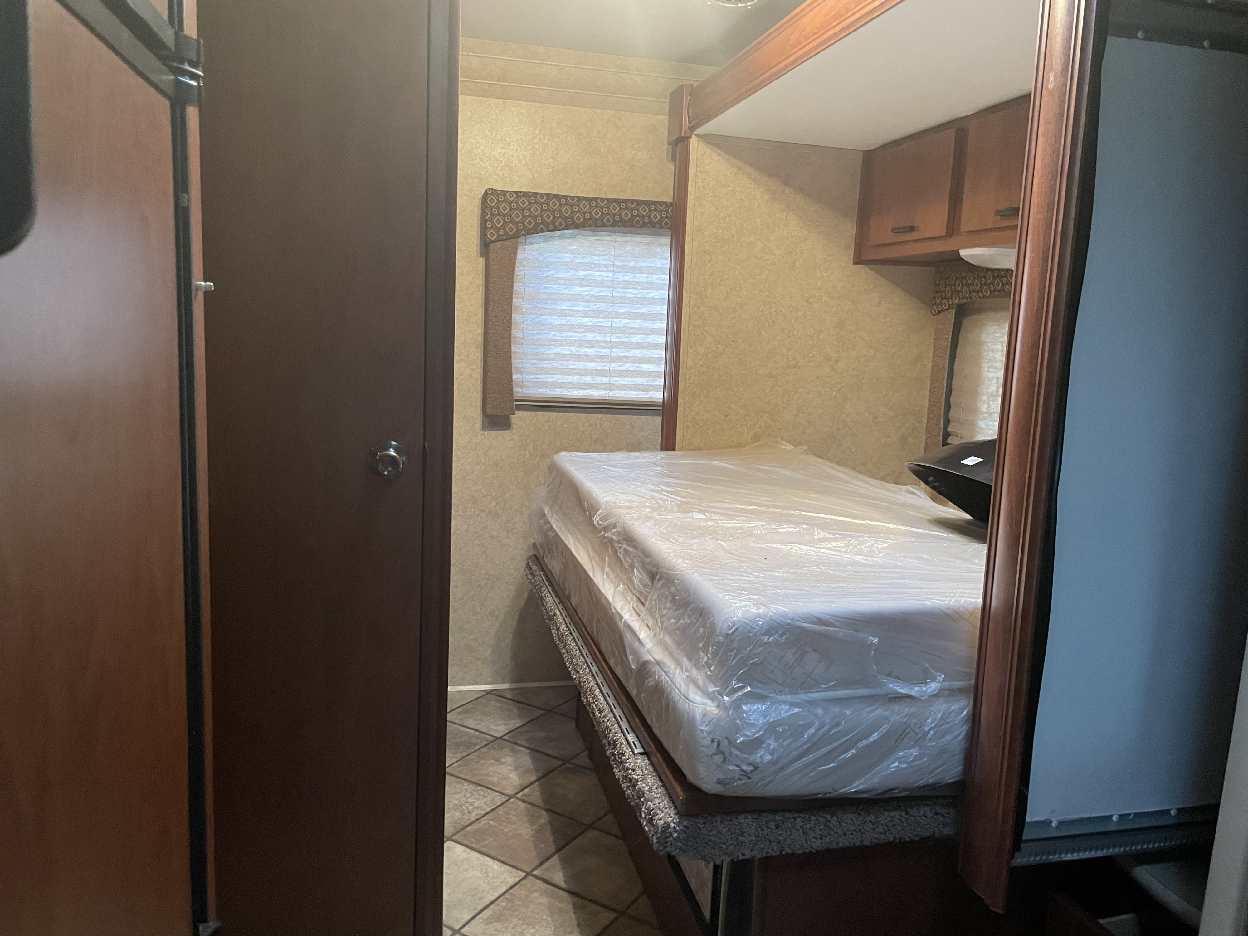 Comfortable RV rental bedroom featuring a new, plastic-wrapped mattress, window with blinds, and overhead storage cabinets.. Forester LE 2012