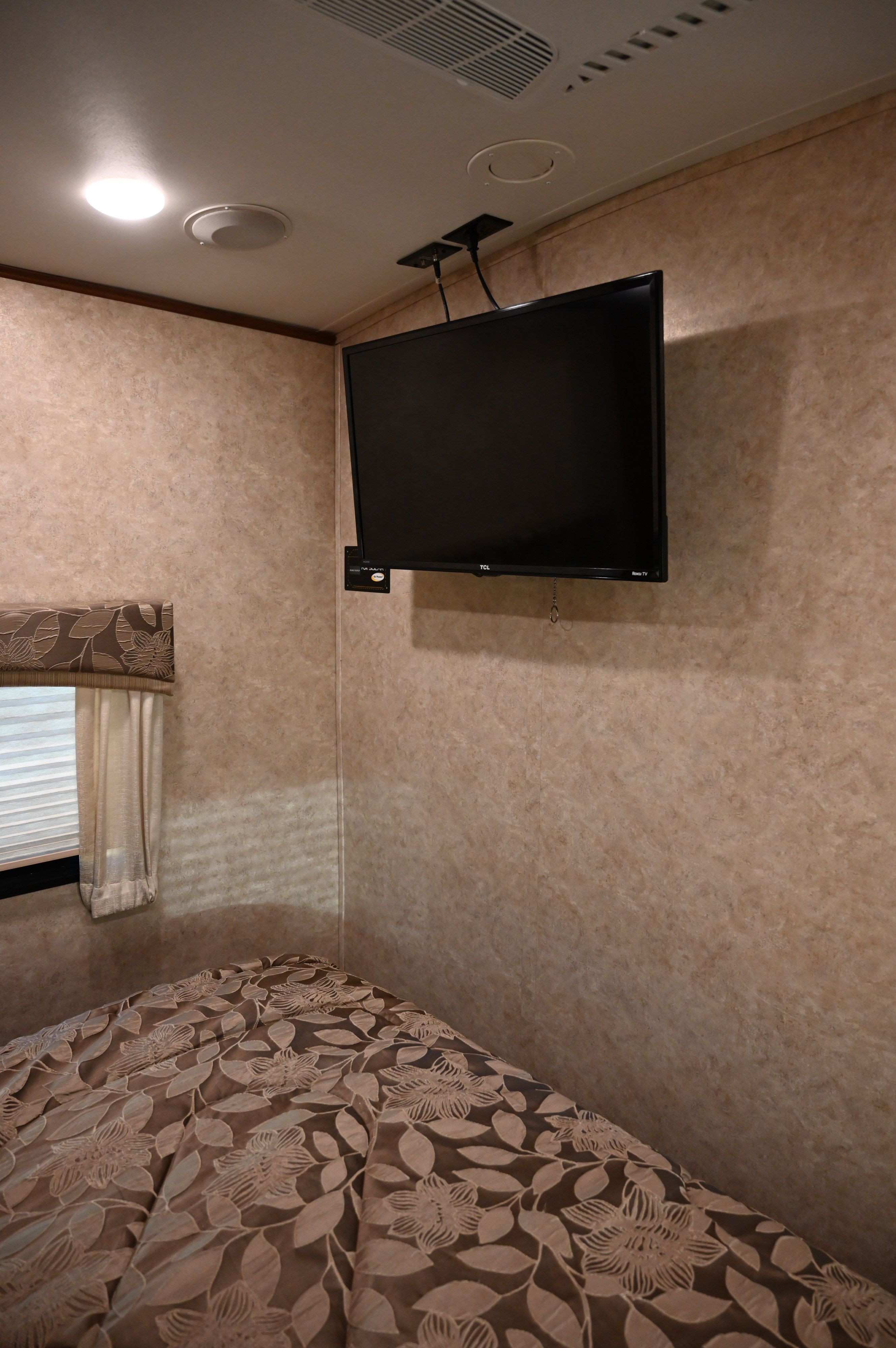RV rental bedroom interior featuring a wall-mounted TV, a bed with floral comforter, and a window with blinds.. Jayco Eagle 2017